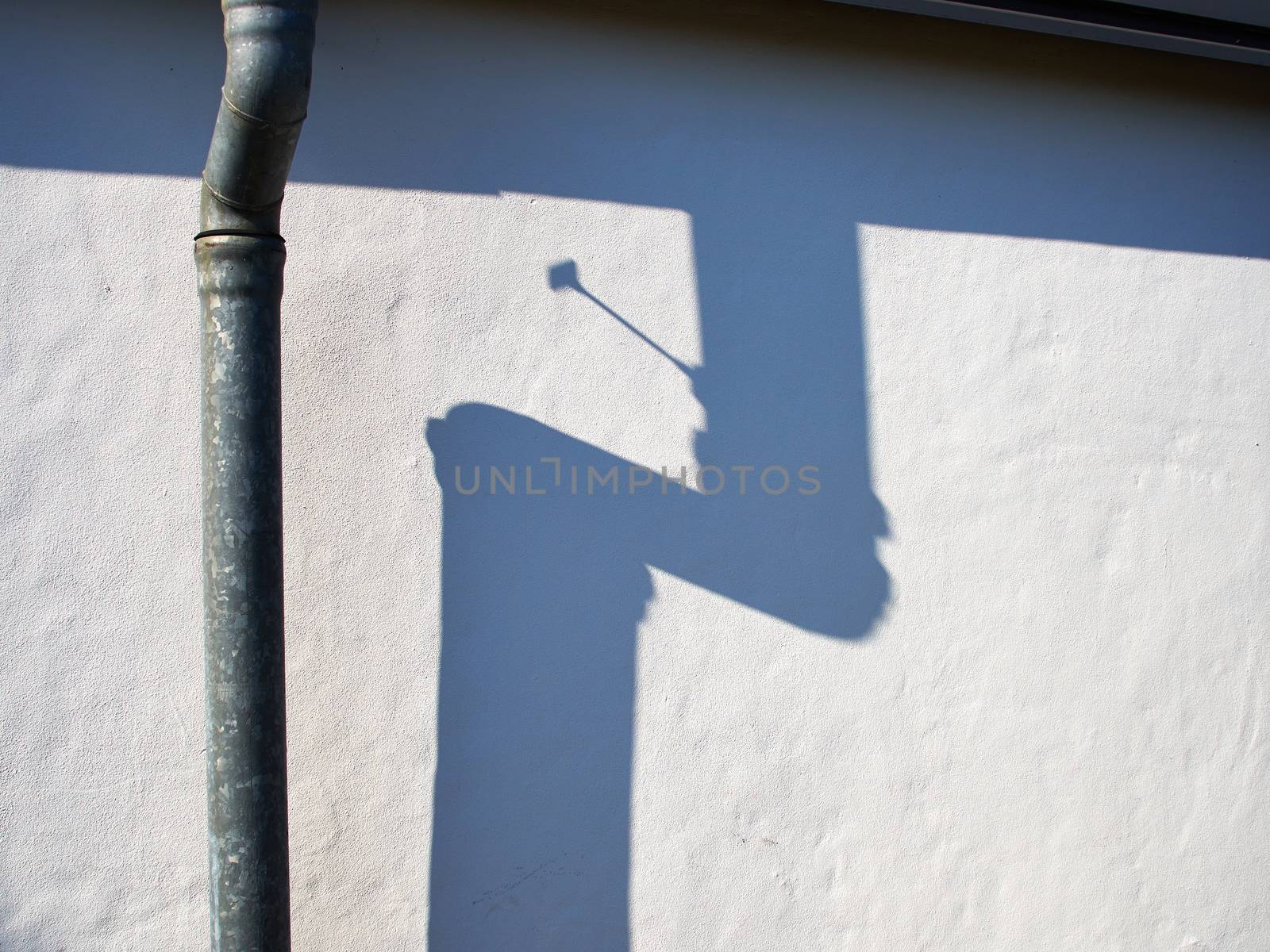 Metal drain pipe against a white wall casting shadow in strong sunlight     