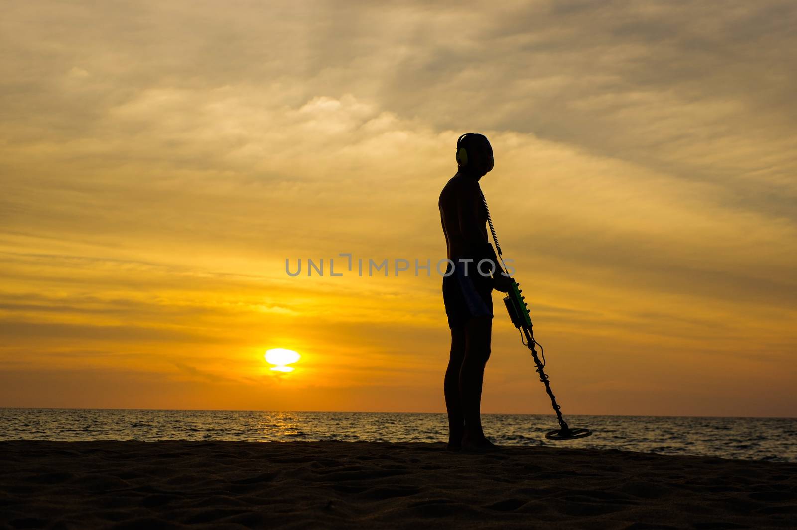 Treasure hunter with Metal detector on sunset  the beach by evolutionnow