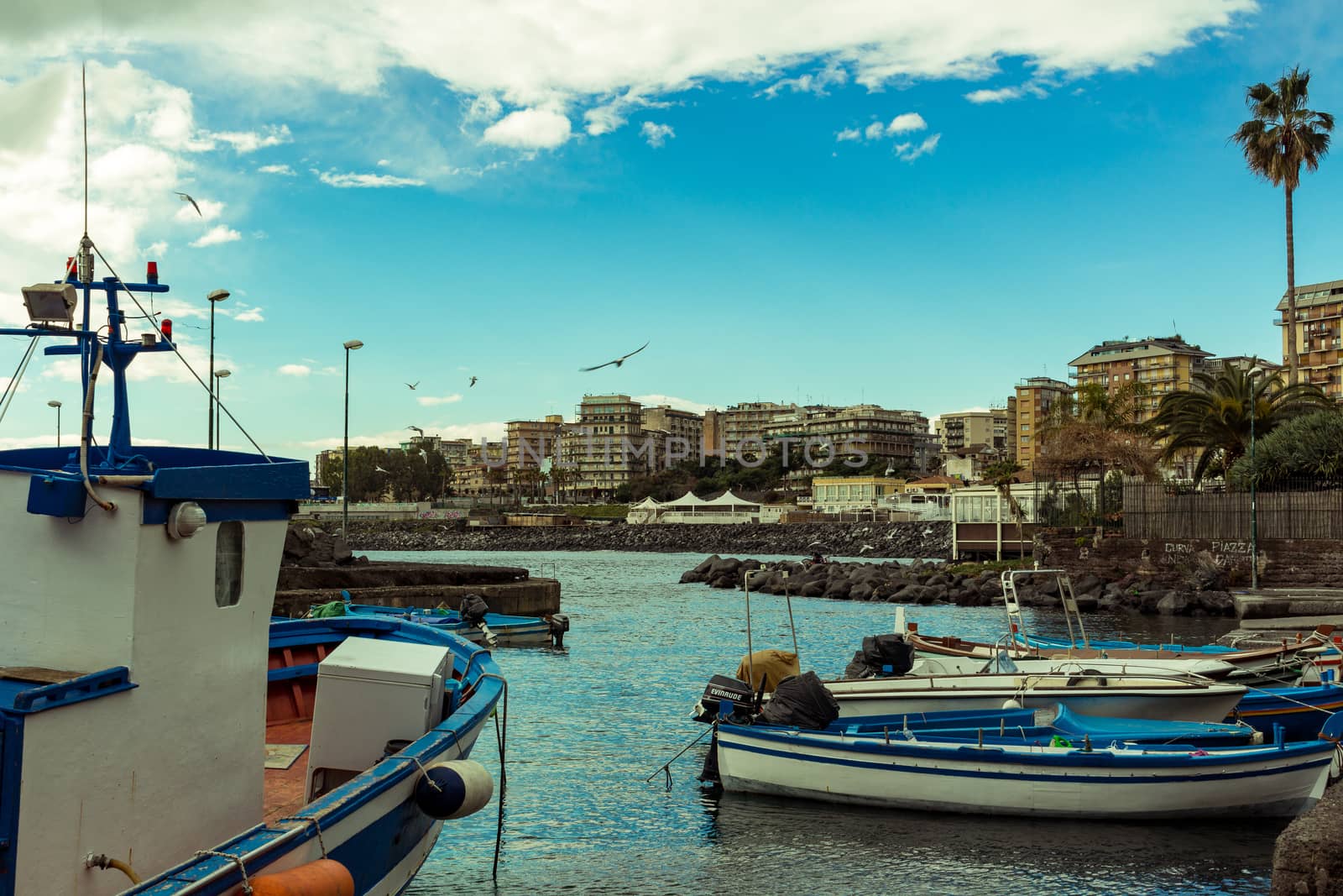 Several small colorful boats are anchored in the harbor of Catania, SIcily-Italy on the coast of the Mediterranean Sea.