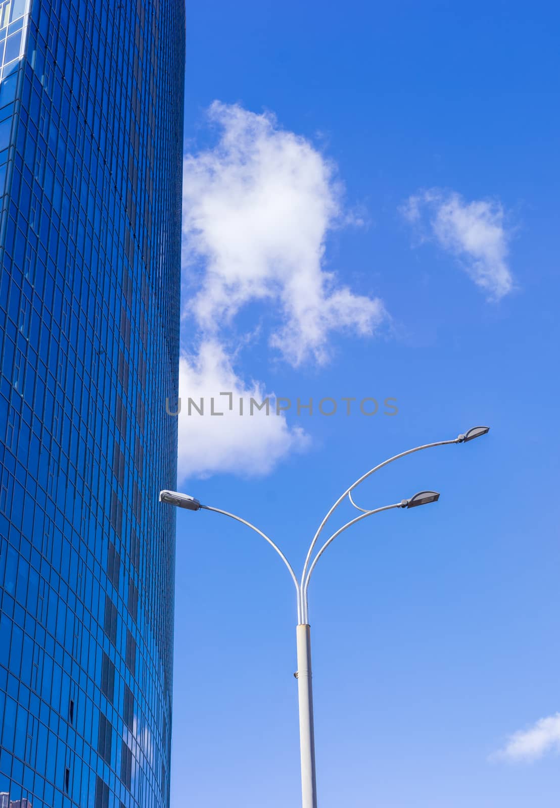 Fragment of the large modern multistory office building and pole of a street lighting against the background of sky with clouds
