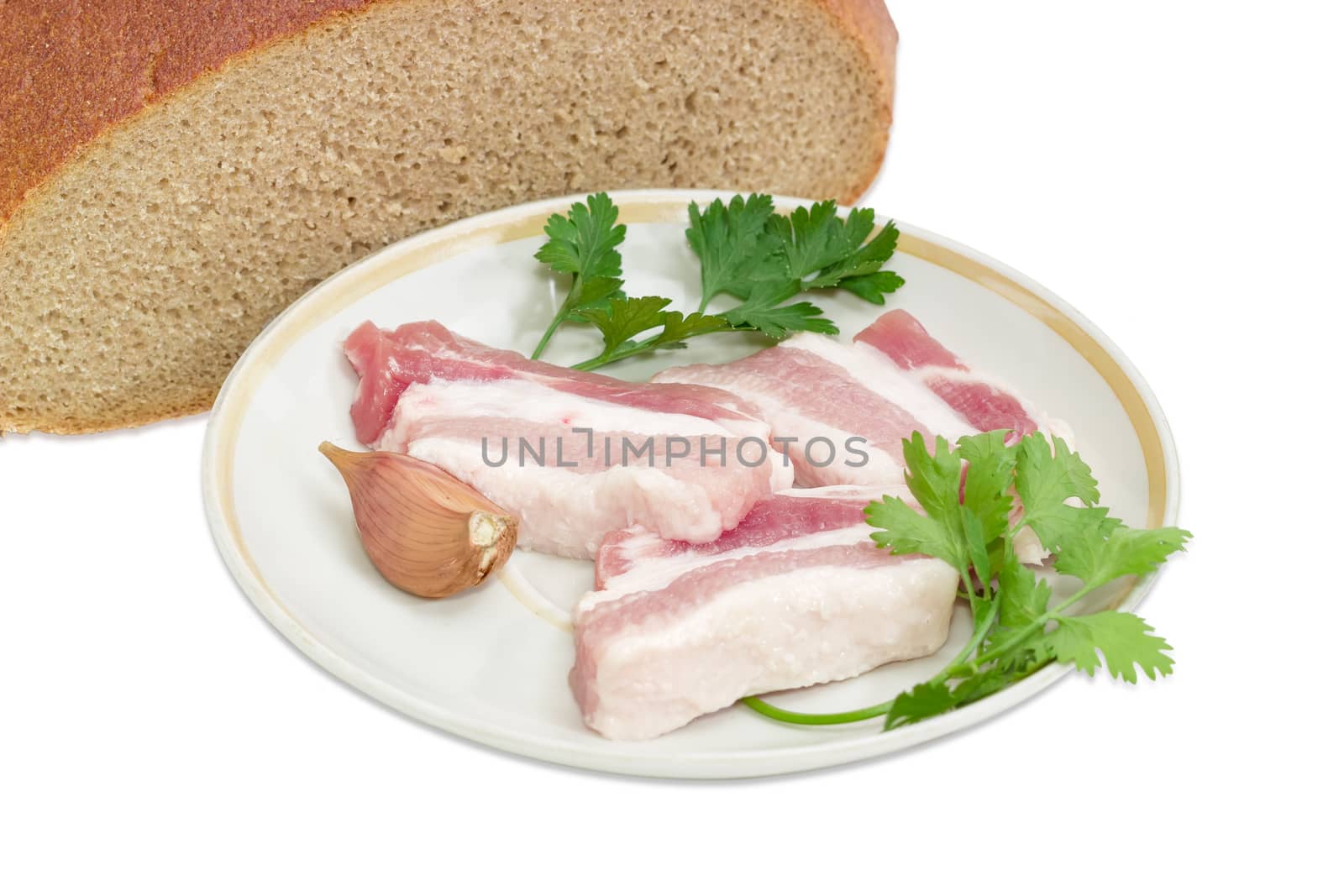 Several slices of uncooked streaky pork belly bacon, garlic, twigs of parsley and cilantro on saucer against the background of cut hearth brown bread closeup on a light background 
