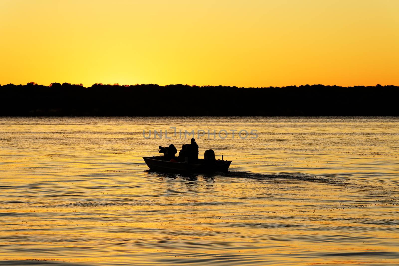 Fishermen boating into the golden sunrise on a reflective lake.