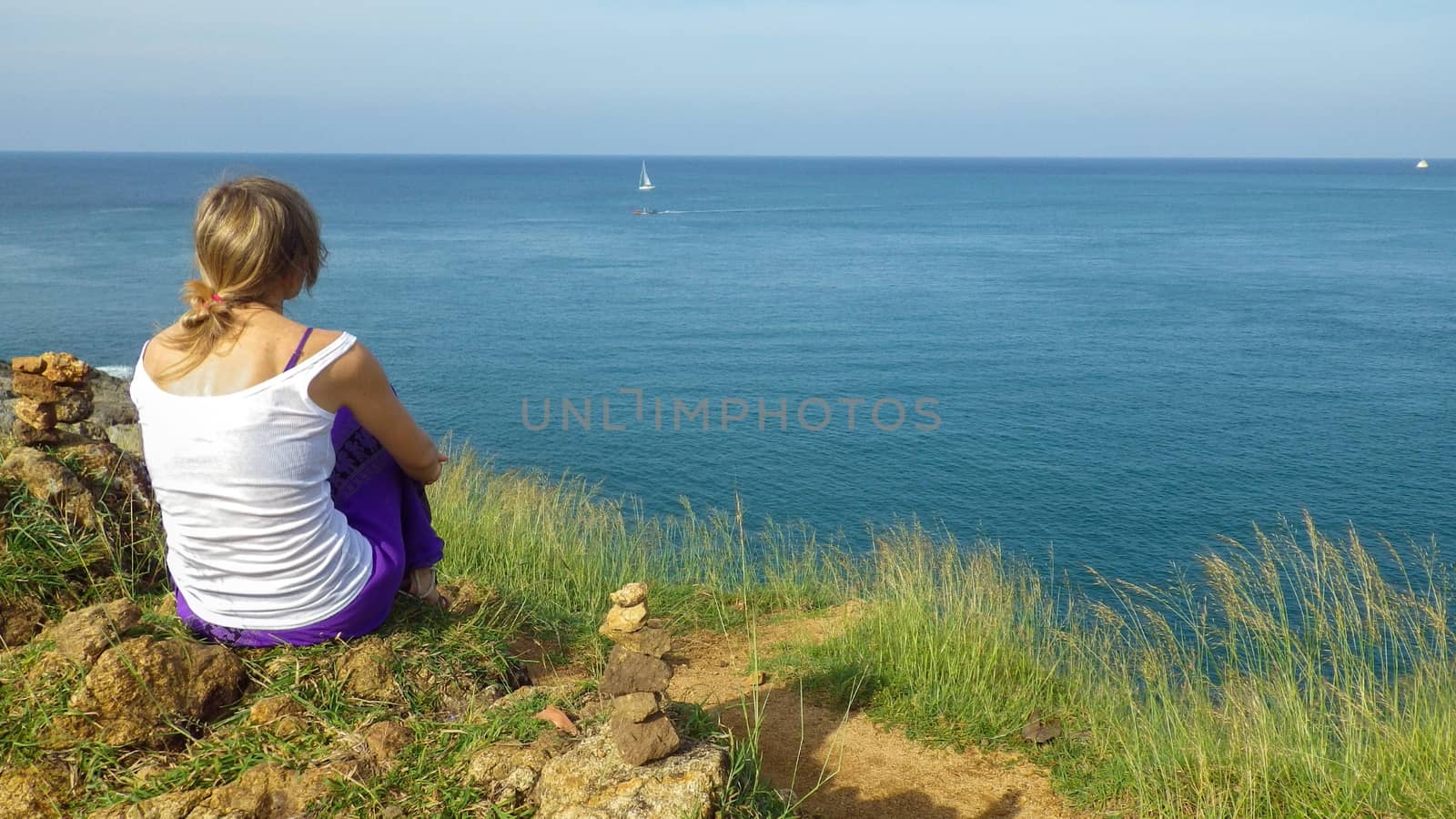 Young woman sits on a hill and looking at the sea. Relax in the solitude of the sea. with nature alone. Enjoying views of the sea landscape scale.