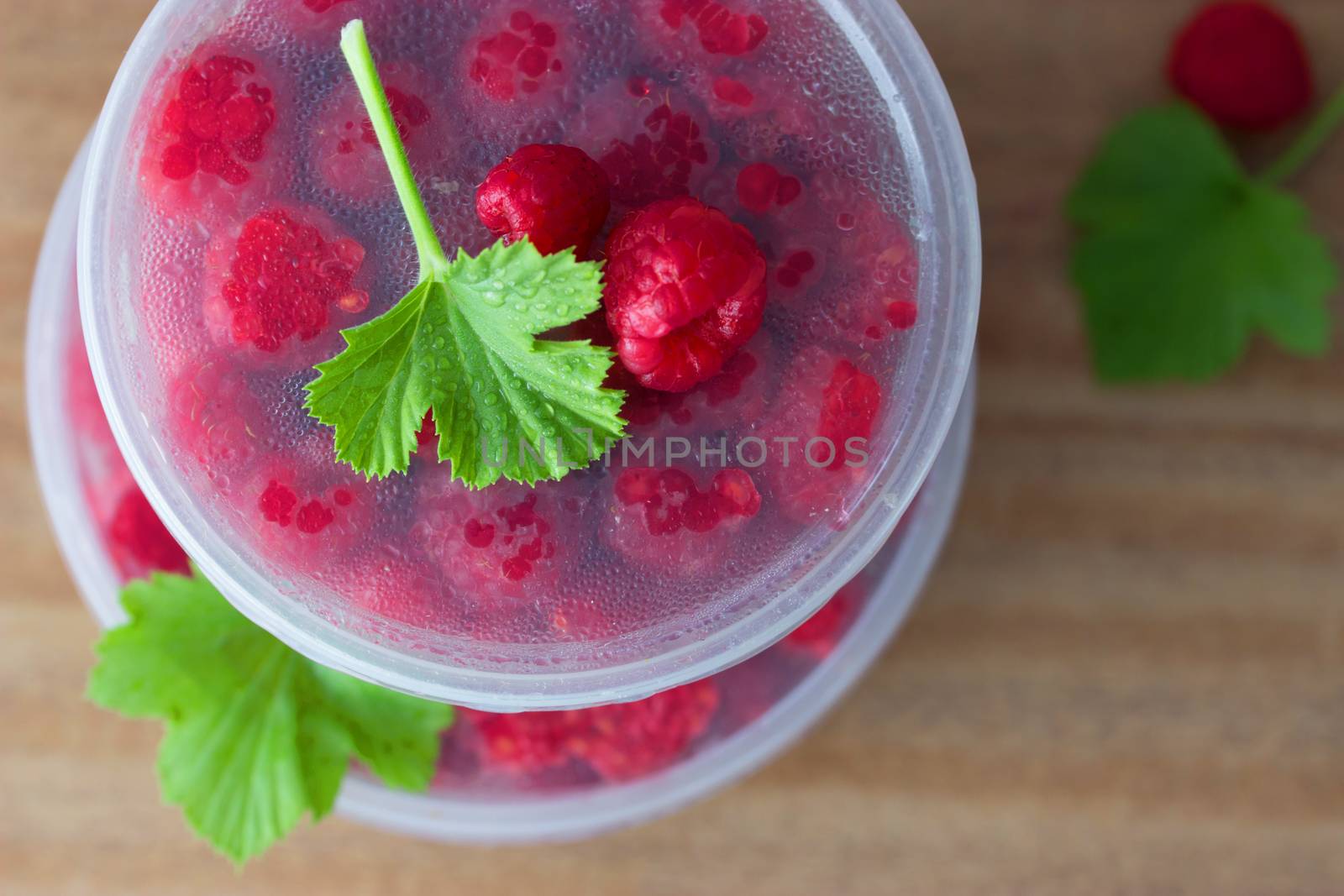 Raspberry in the round box with leaf of mint on the old wood background