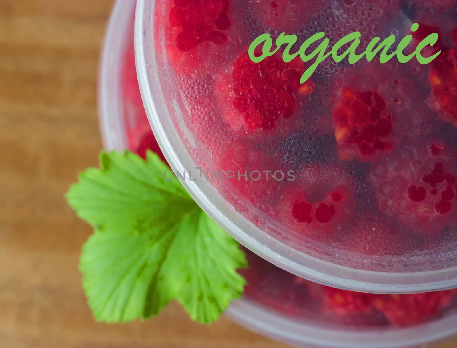 Raspberry in the round box with leaf of mint on the old wood background