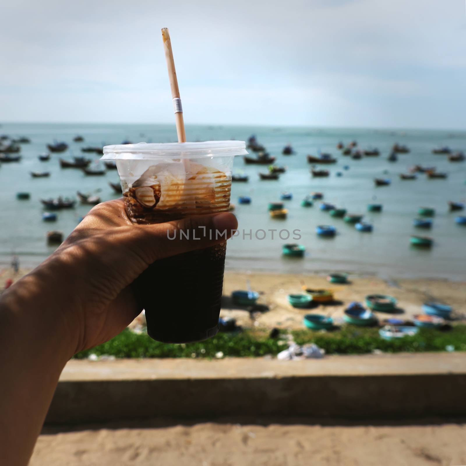 Woman hand hold coffee cup up to sky at beach in morning, quick cafe time on the way in summer journey to enjoy life