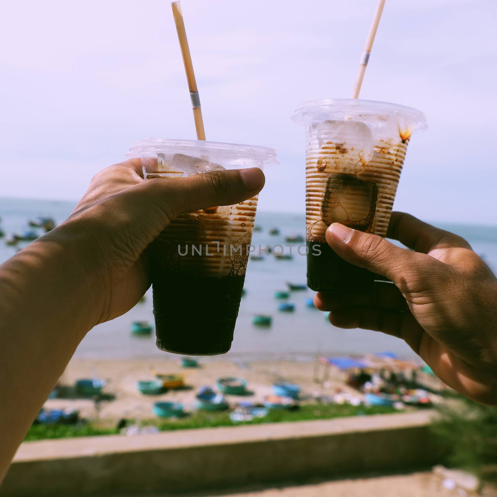 Couple hand hold coffee cup up to sky at beach in morning, quick cafe time on the way in summer journey to enjoy life