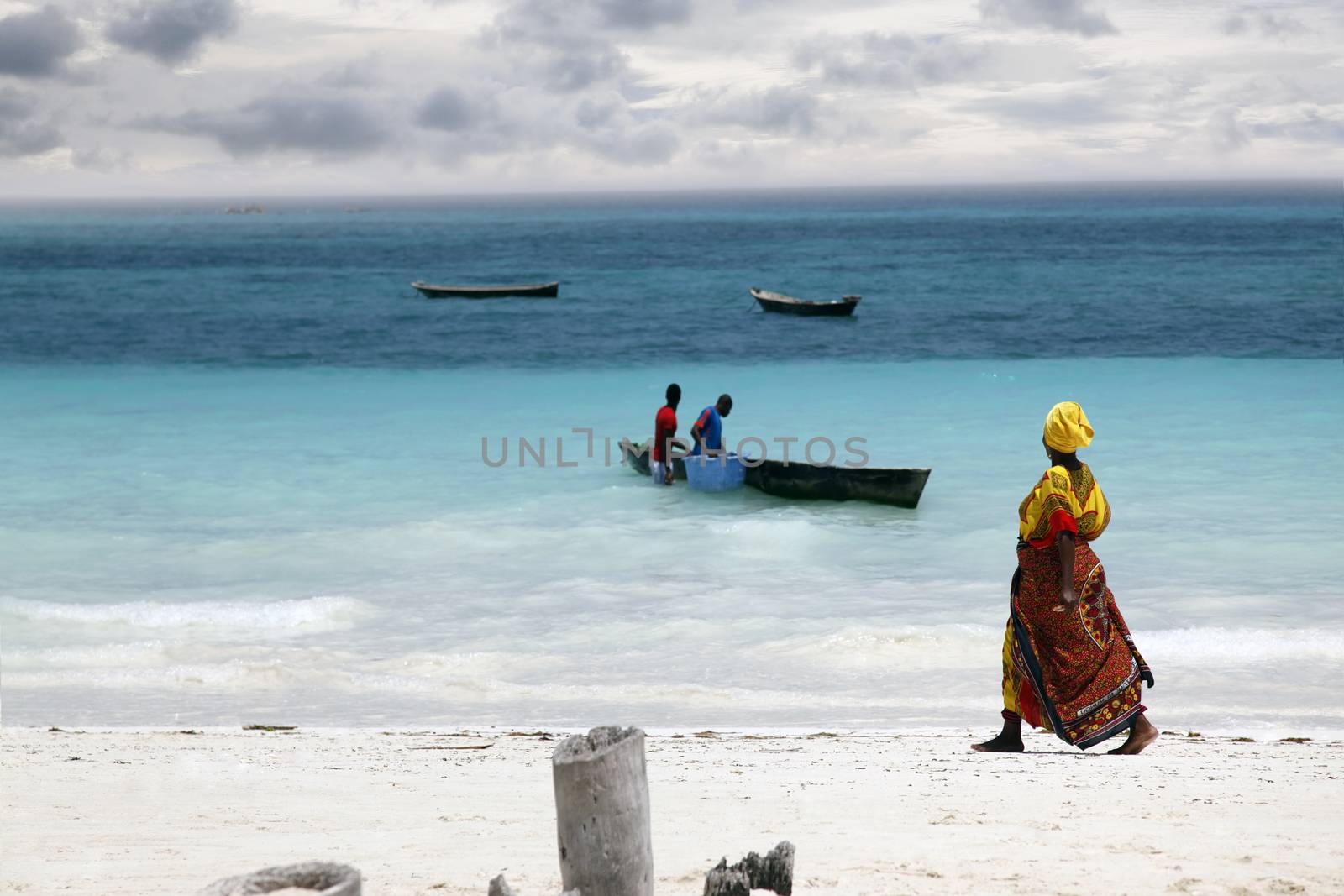Zanzibar, Tanzania - January 7, 2016: An African woman in traditional dress with fish walks down the beach. Zanzibar, Tanzania