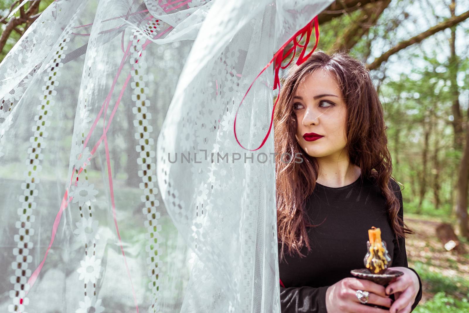 mysterious woman witch in the forest with a candle hidden behind the curtains