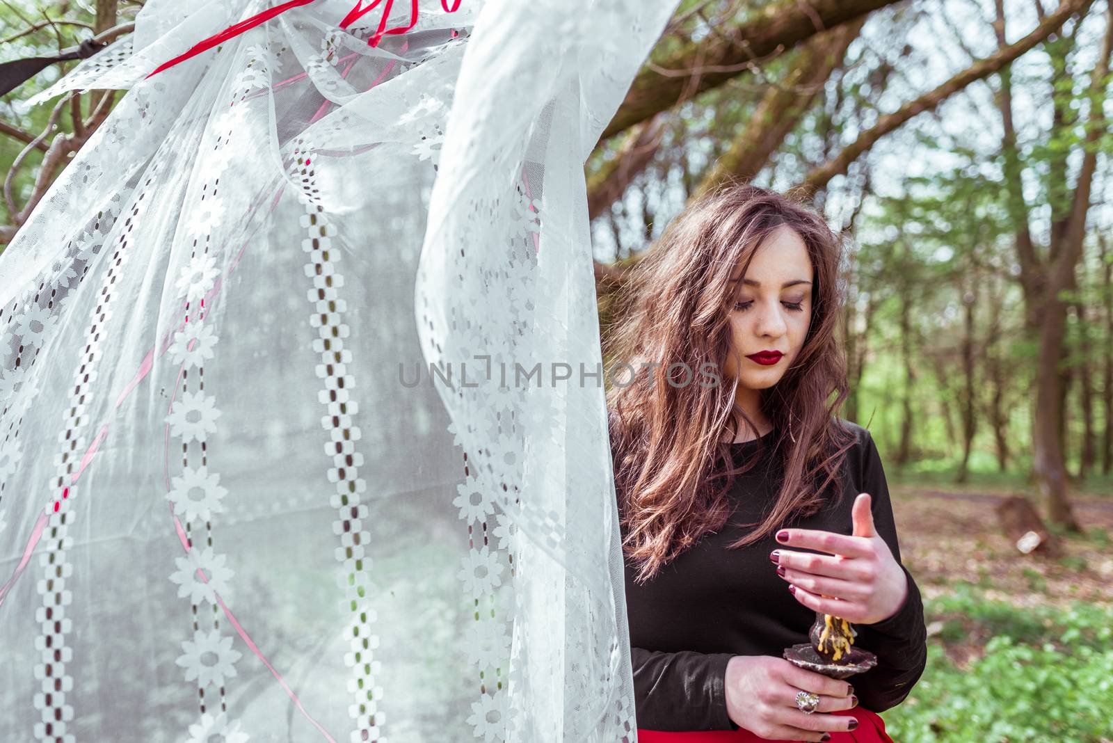 mysterious woman witch in the forest with a candle hidden behind the curtains