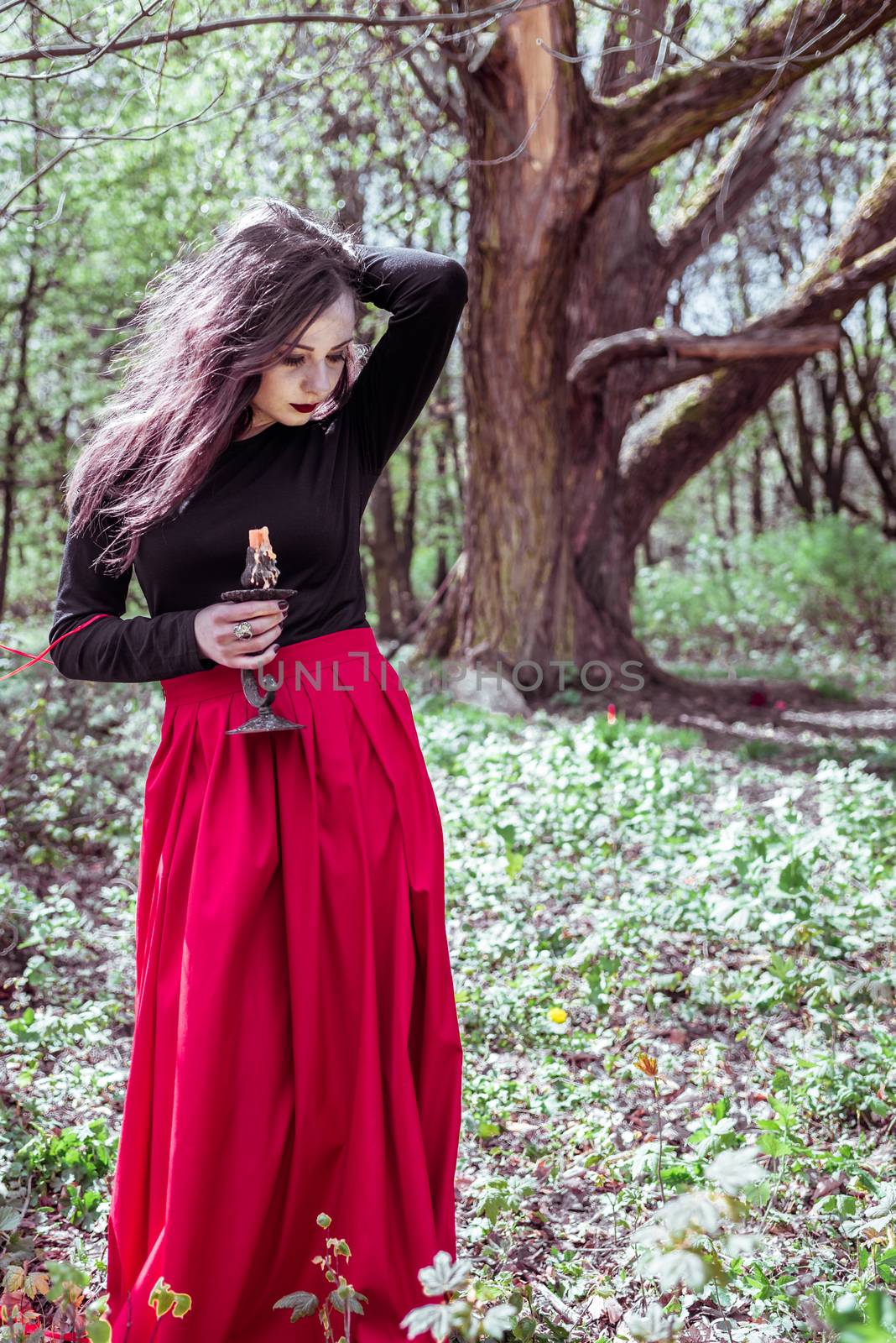 mystical witch woman in a red skirt with a candle in spring forest