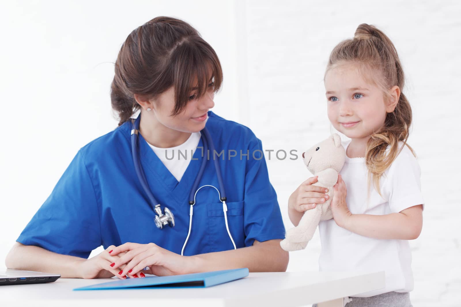 Young smiling female doctor and her little patient with teddy bear