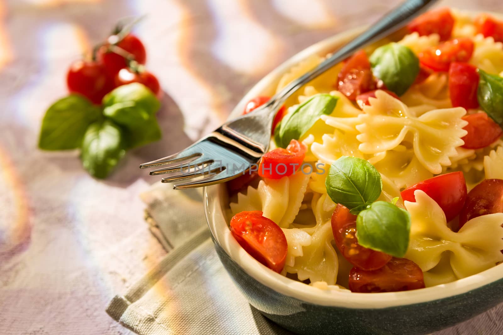 Closeup of Italian Farfalle pasta with tomatoes, basil and fork over a colored background
