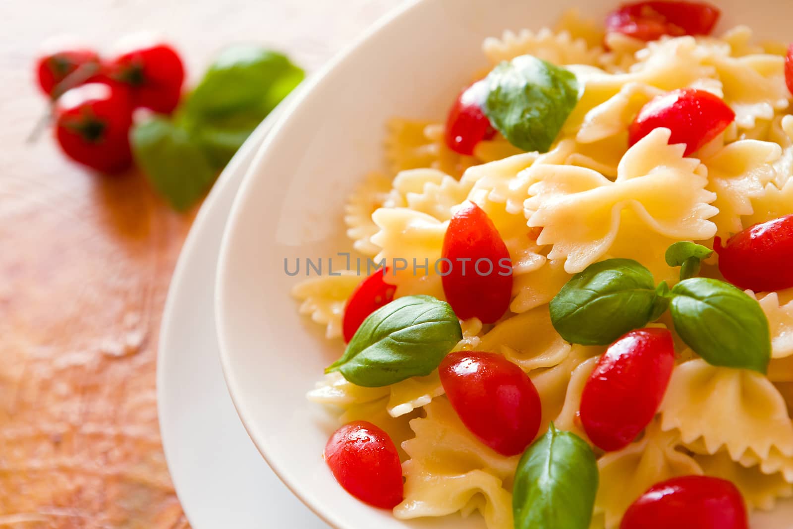 Closeup of Farfalle pasta with cherry tomatoes and basil over a colored background