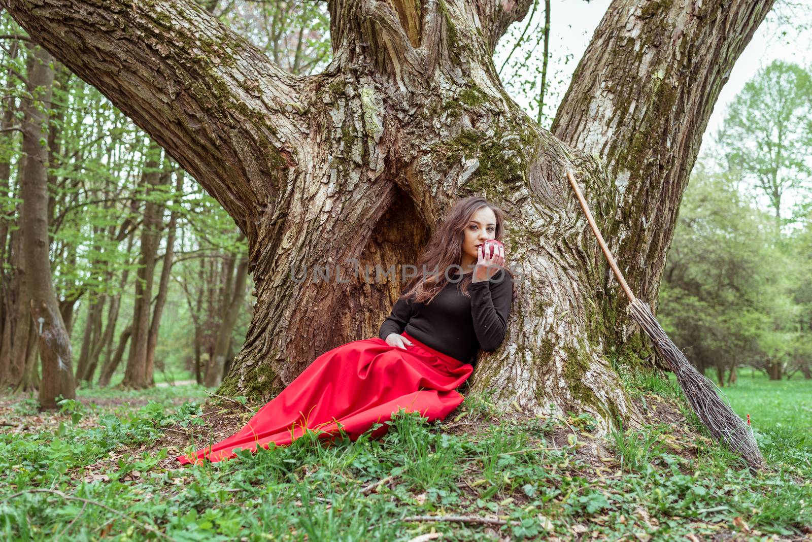 mystical witch woman sitting under a old tree in the spring forest