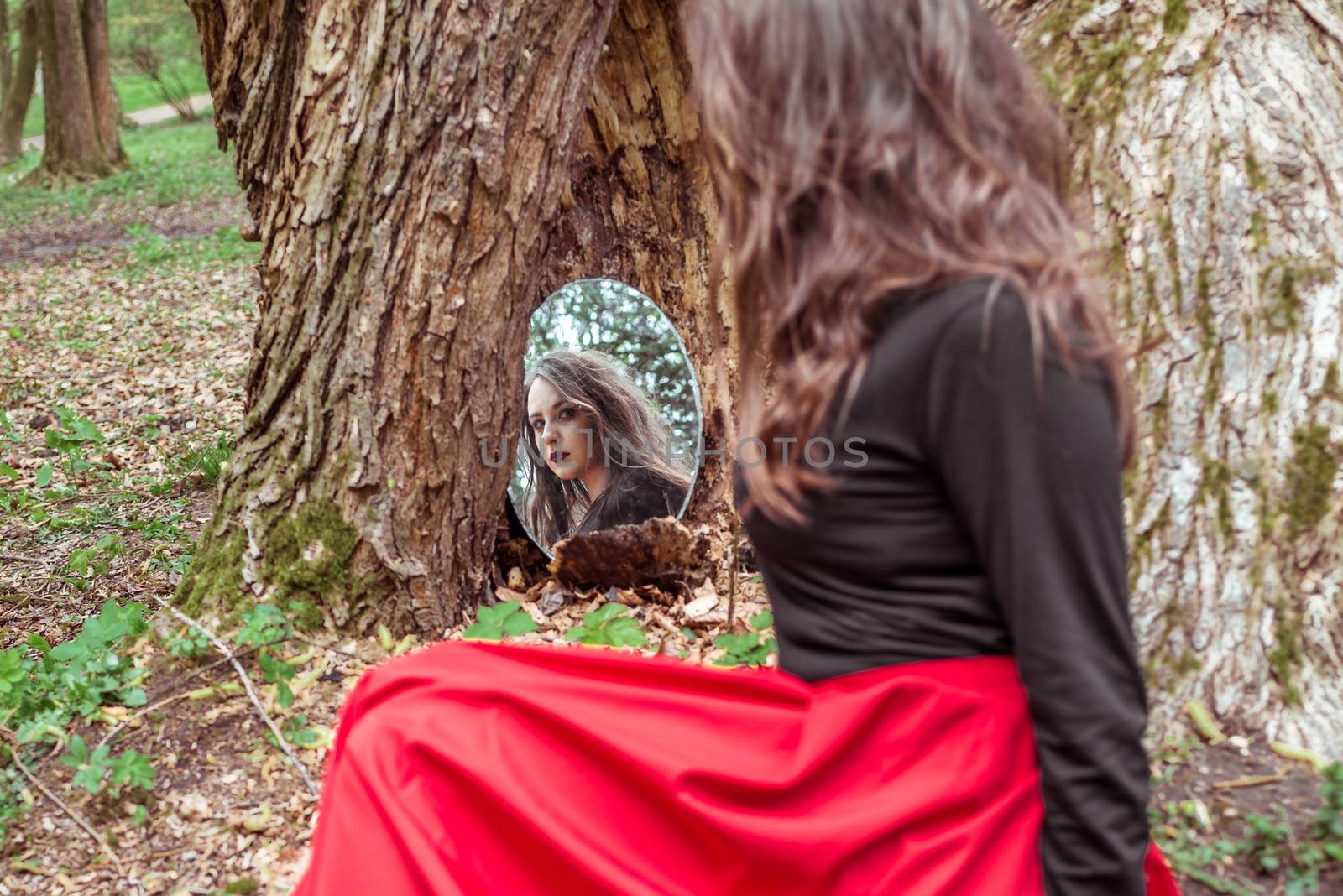 mystical woman looks in the mirror near a tree at the spring forest