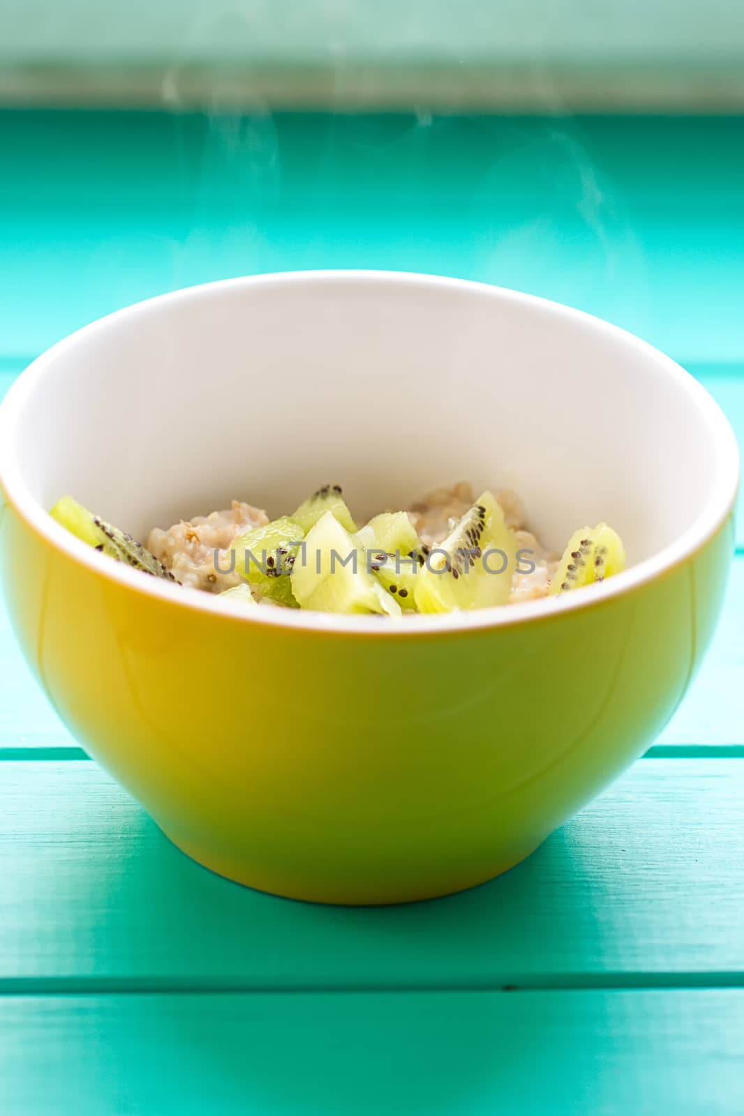 Oatmeal with milk and kiwi in a yellow bowl by victosha