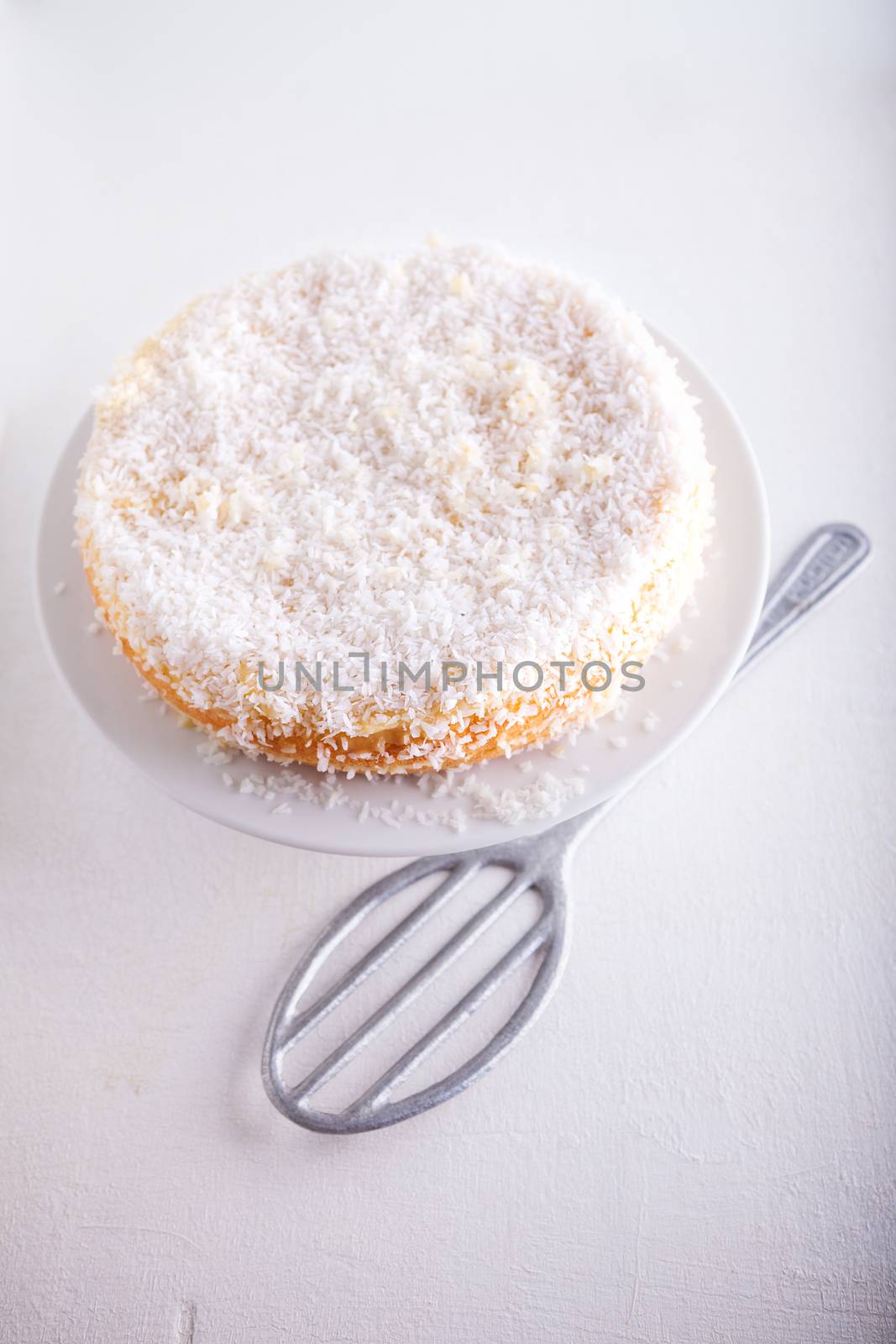 Homemade coconut cake with a spoon on a white surface