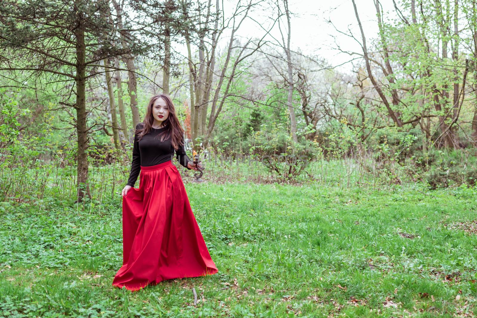 mystical witch woman in a red skirt with a candle in spring forest