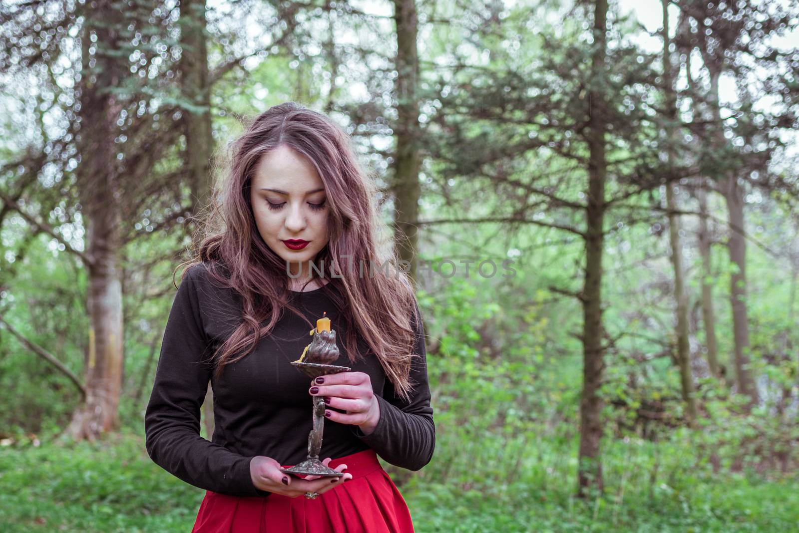 mystical witch woman in a red skirt with a candle in spring forest