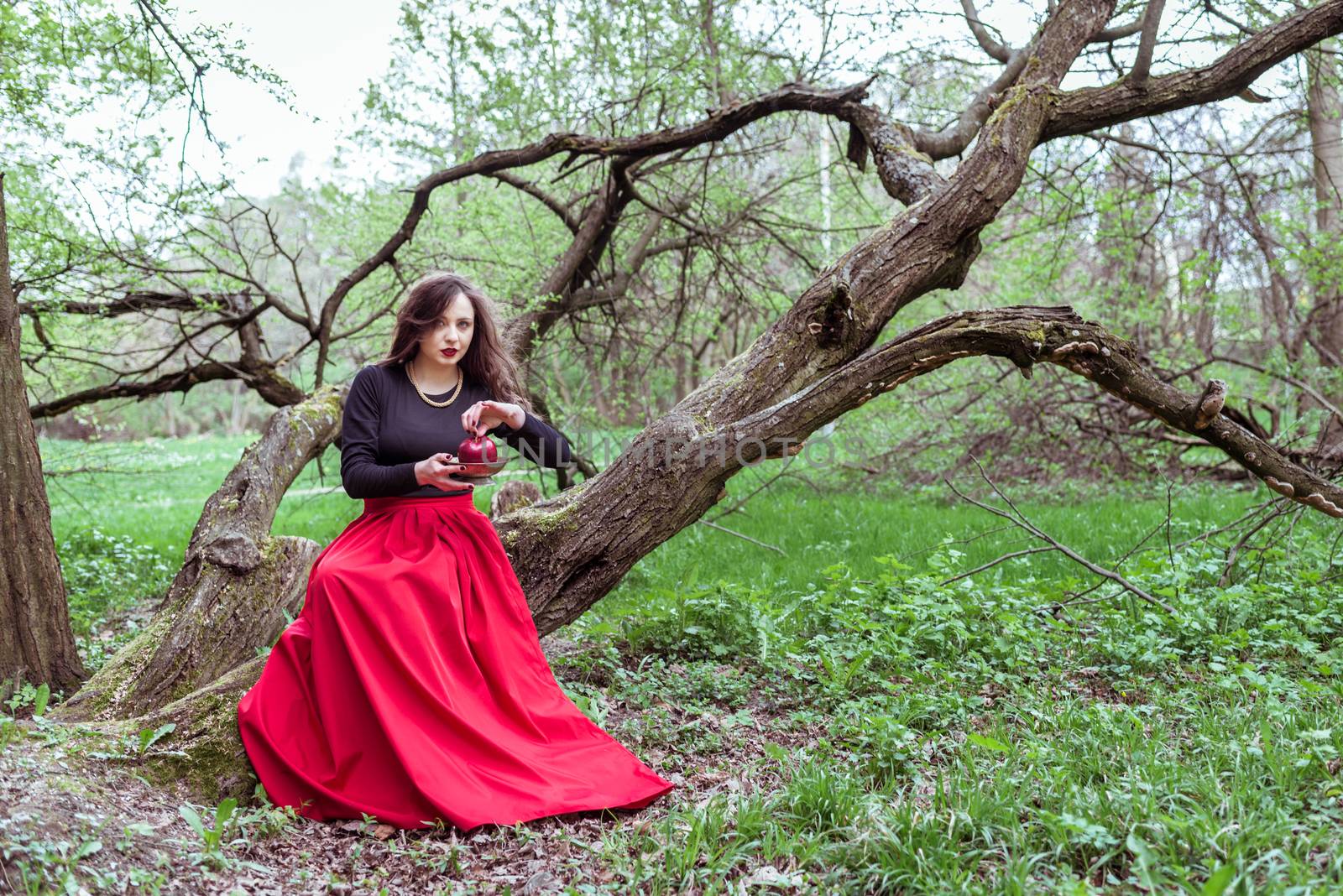 girl in a red skirt sitting on a tree trunk with apple in hand