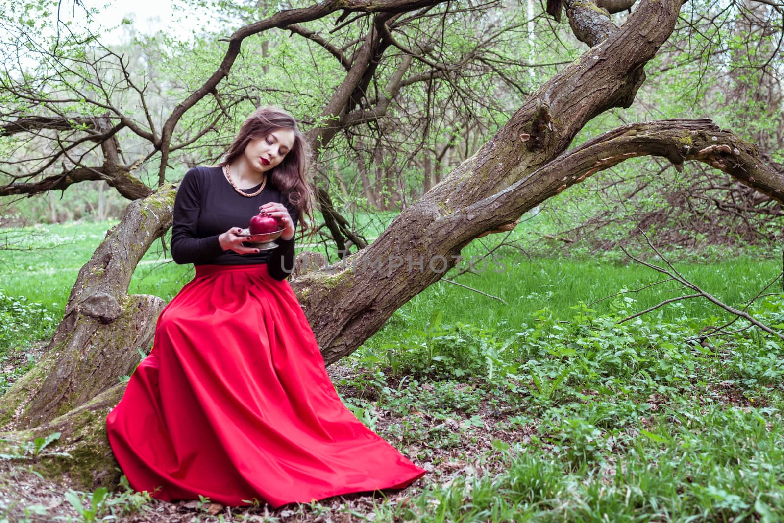 girl in a red skirt sitting on a tree trunk with apple in hand