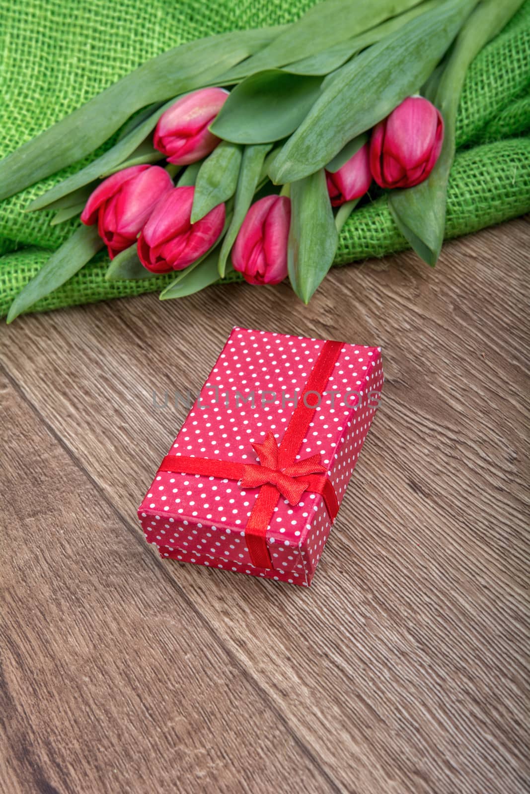 Red tulips and red gift on a wooden background