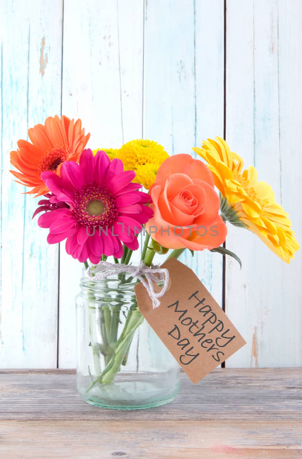 Bunch of flowers with happy mothers day gift label on wooden background