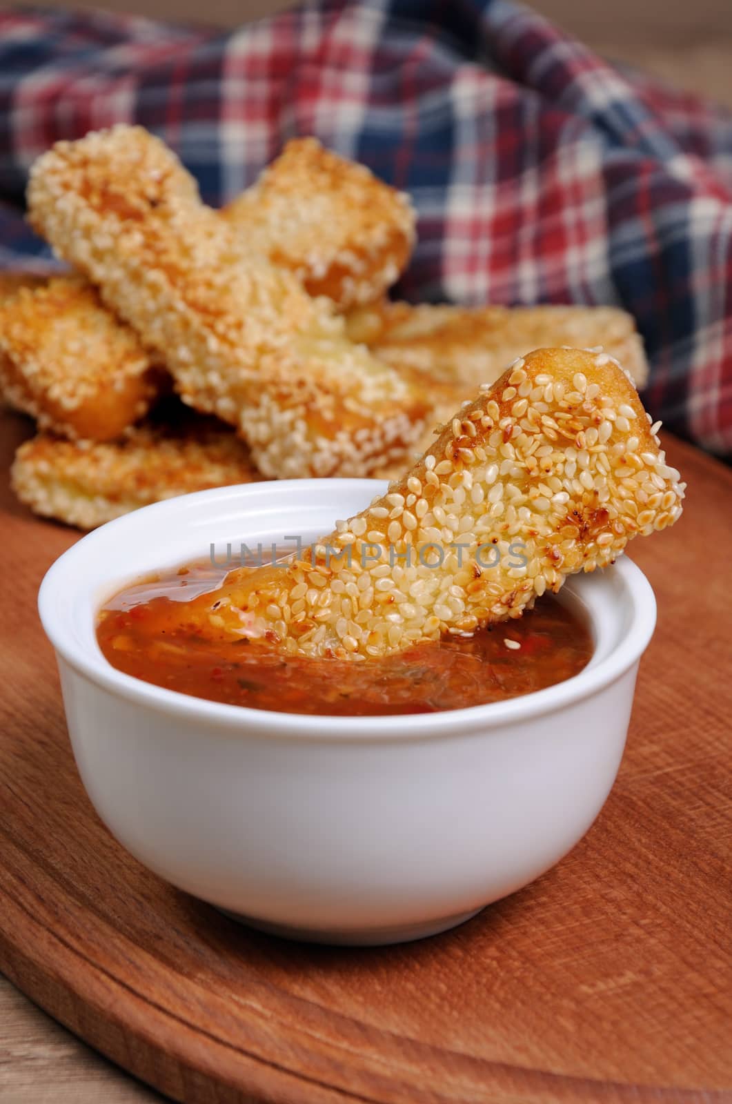 Slice of toast roasted in breaded with cheese and sesame slipped in a sauce on a wooden board