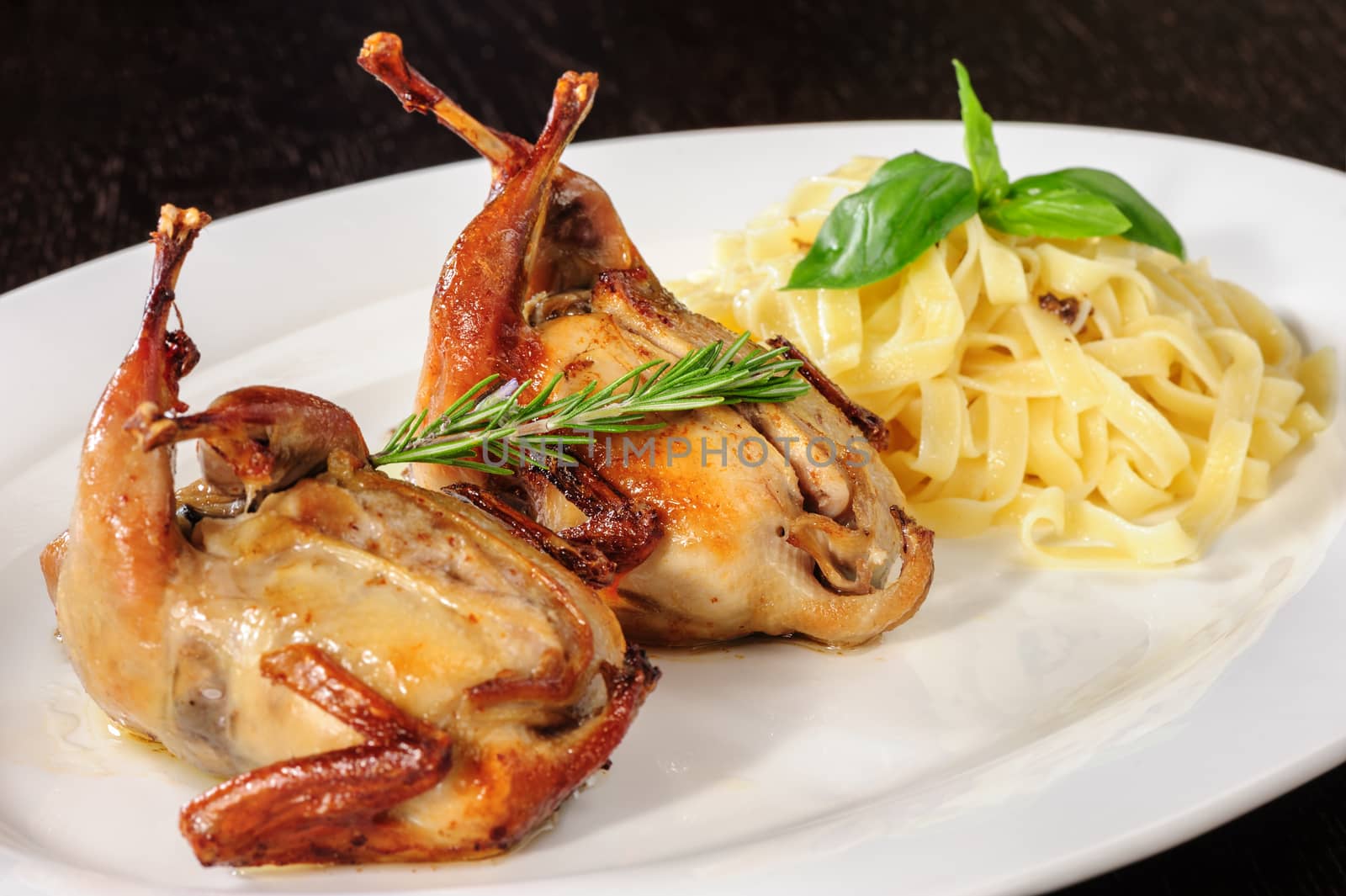 Rosted or fried quail with herbs and tagliatelle at white plate on wooden table