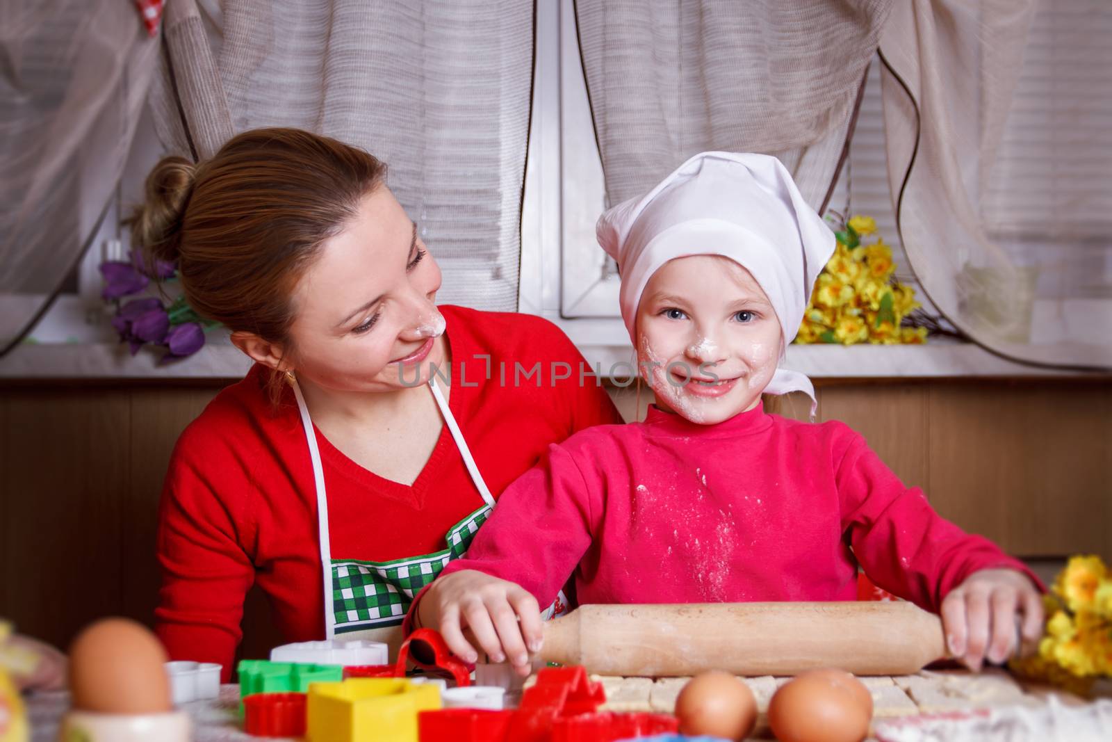 Cute girl rolling dough with her mother
