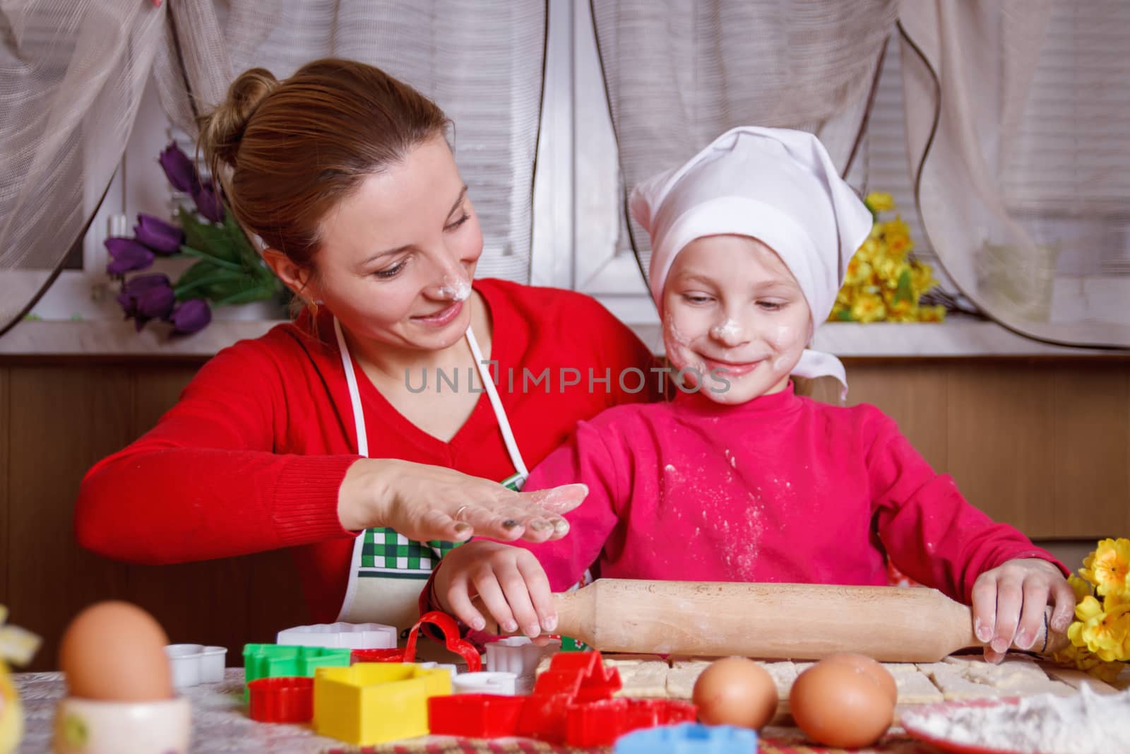 Cute girl rolling dough with her mother for bisquit