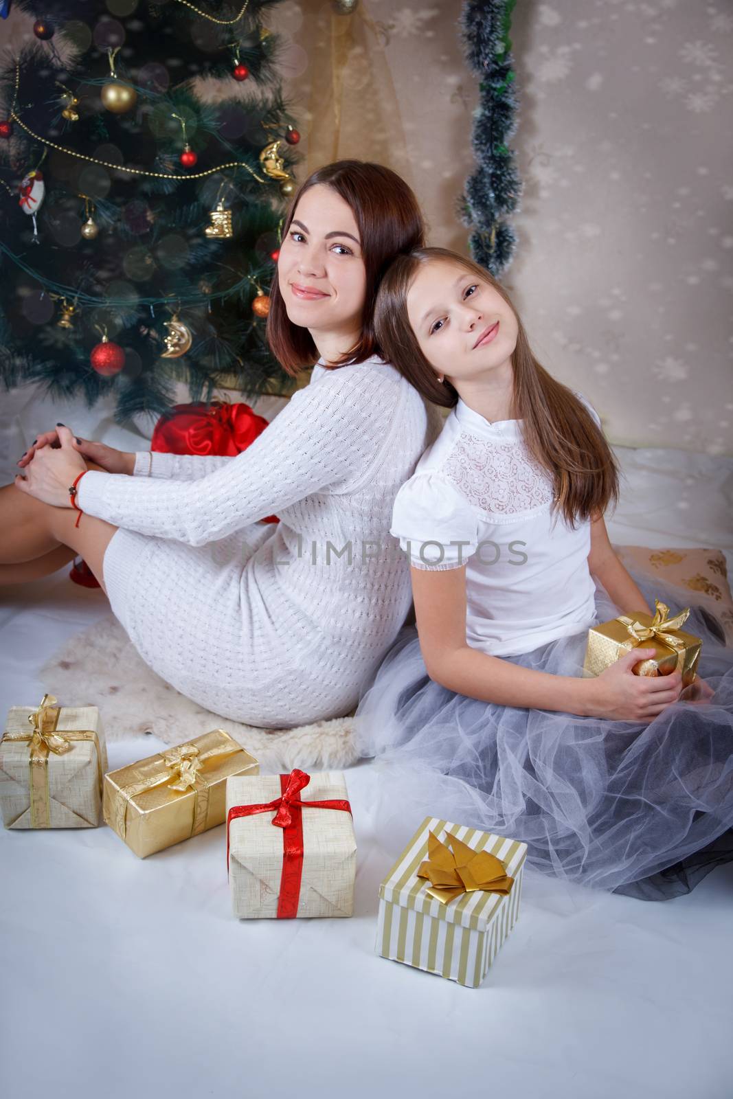Mother and daughter sitting back-to-back under christmas tree