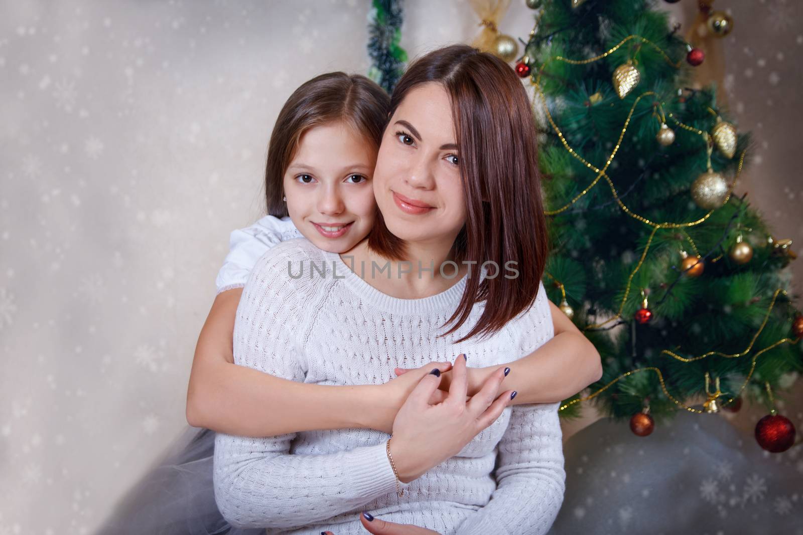 Adorable mother and daughter hugging under Christmas tree