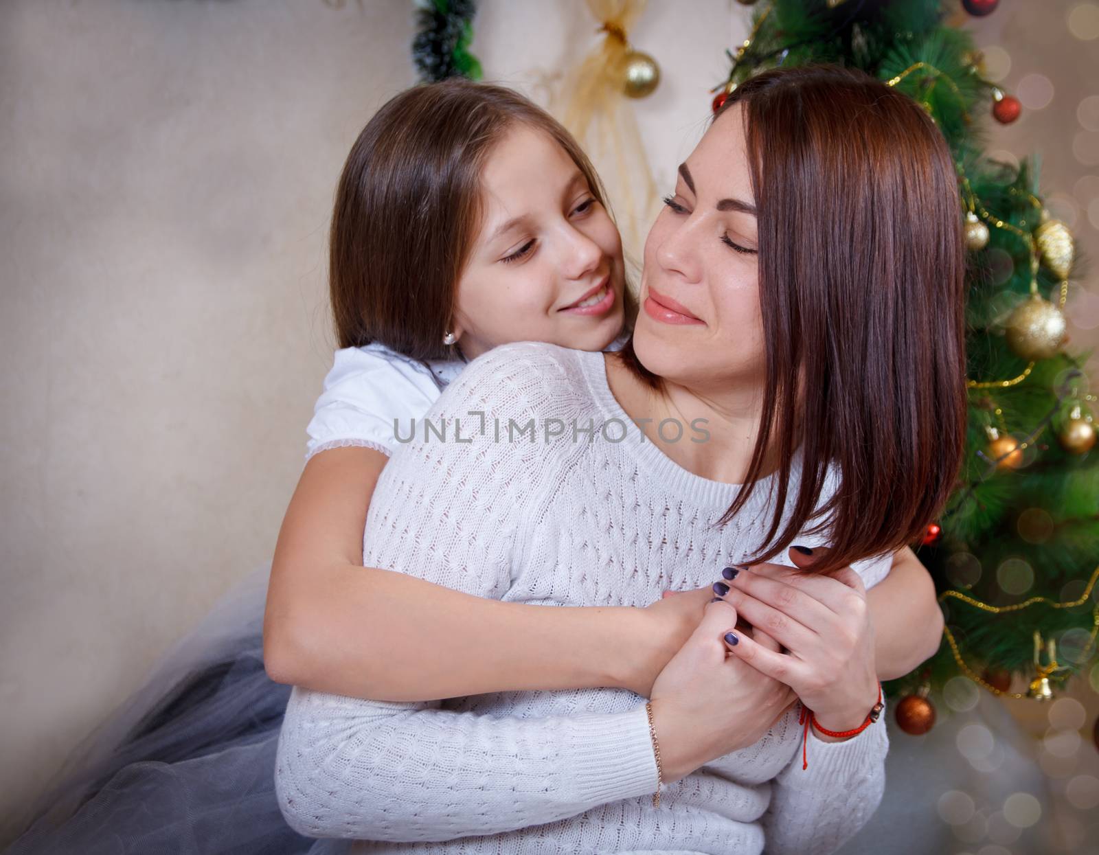 Daughter hugging mother under Christmas tree