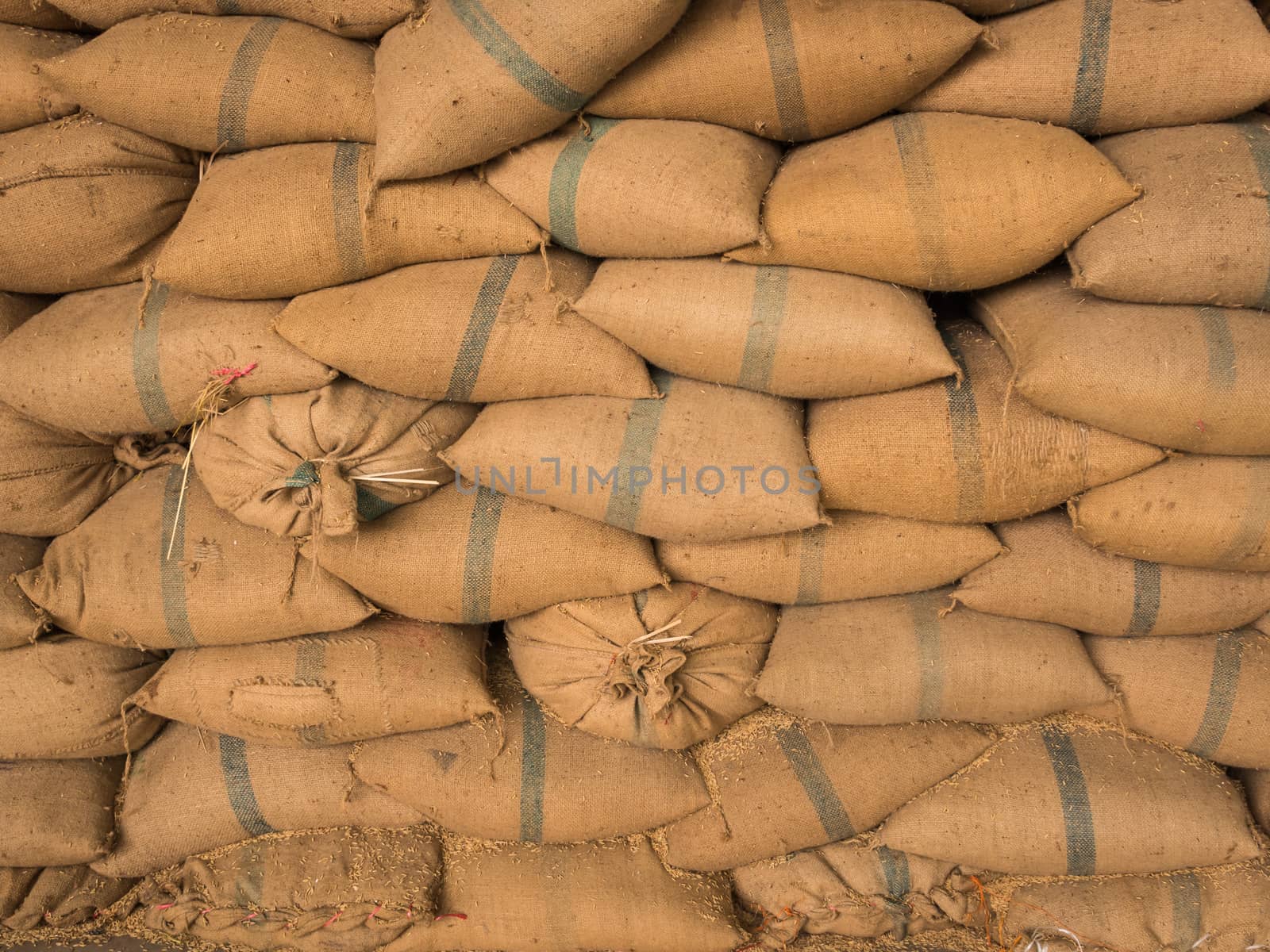 Old hemp sacks containing rice placed stacked in a row.