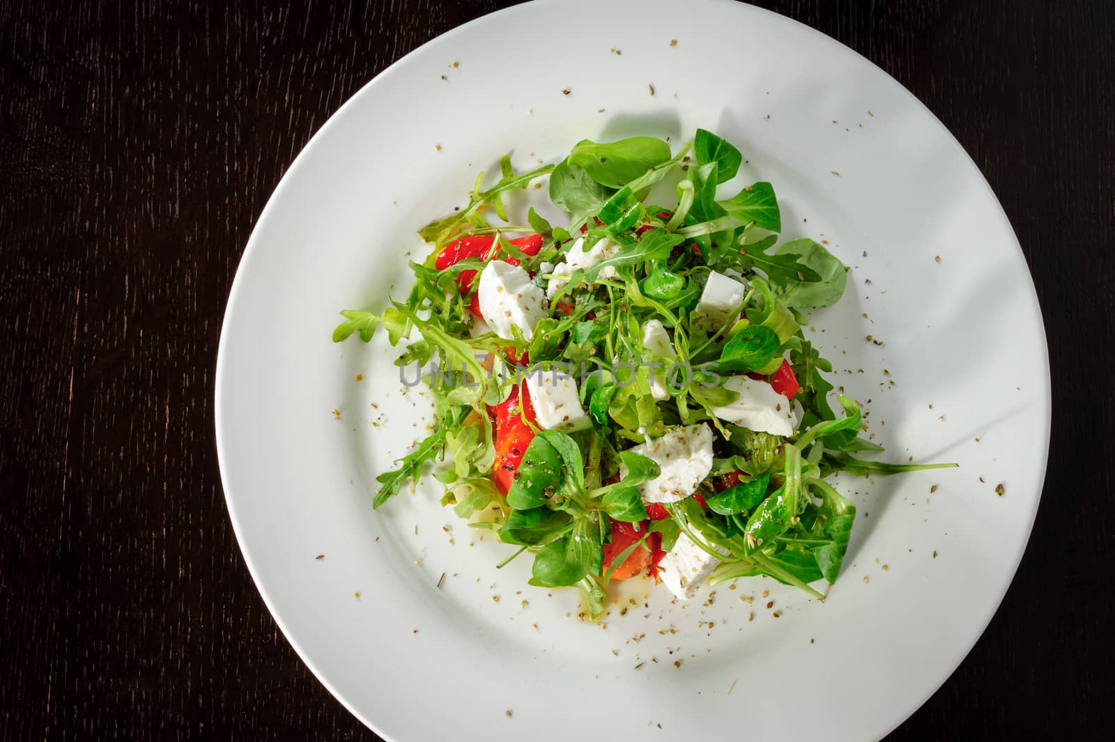 Warm salad with Tomatoes, ruccola, spinach, cooked bell pepper and cheese served on white plate