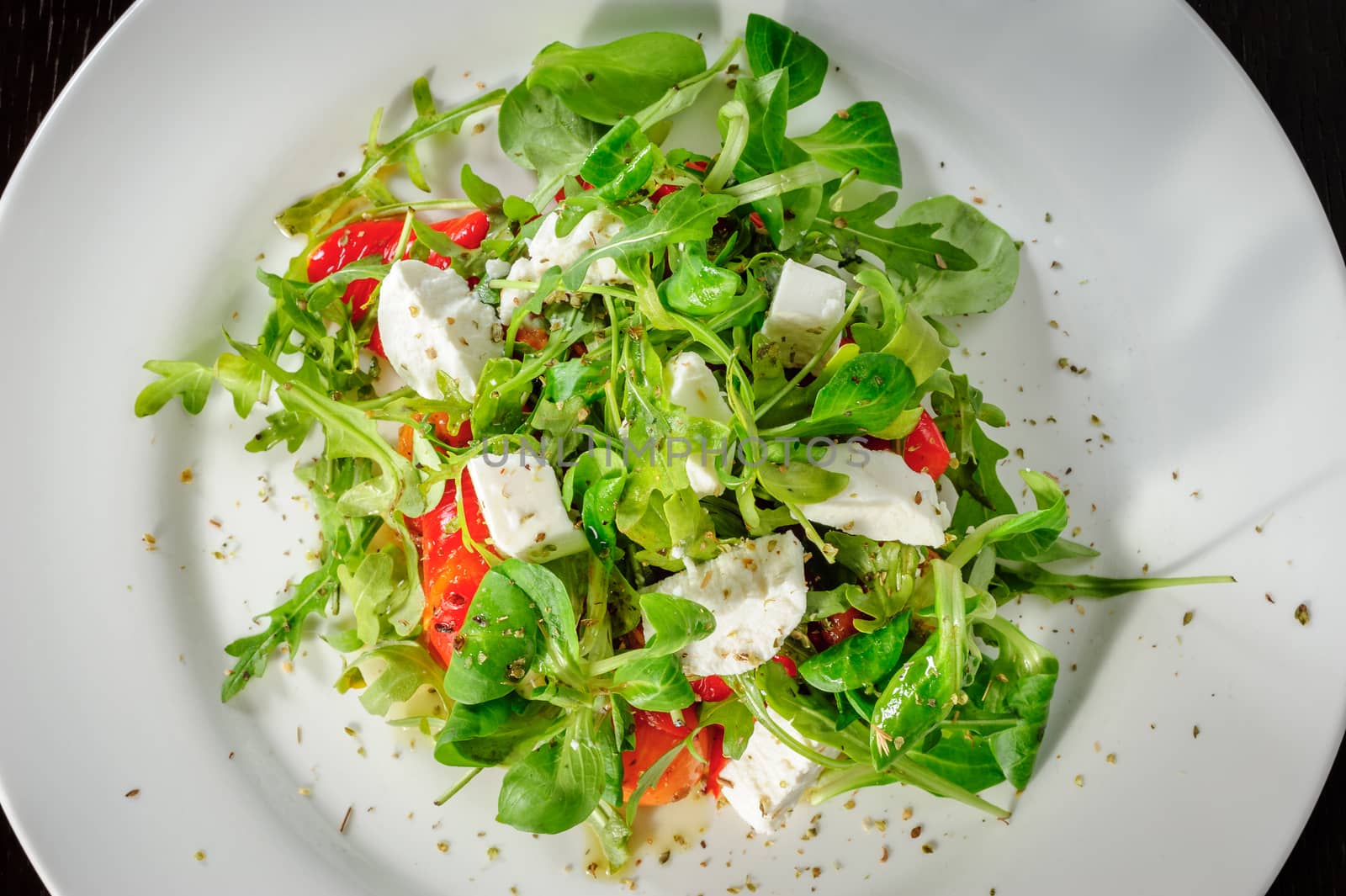 Warm salad with Tomatoes, ruccola, spinach, cooked bell pepper and cheese served on white plate