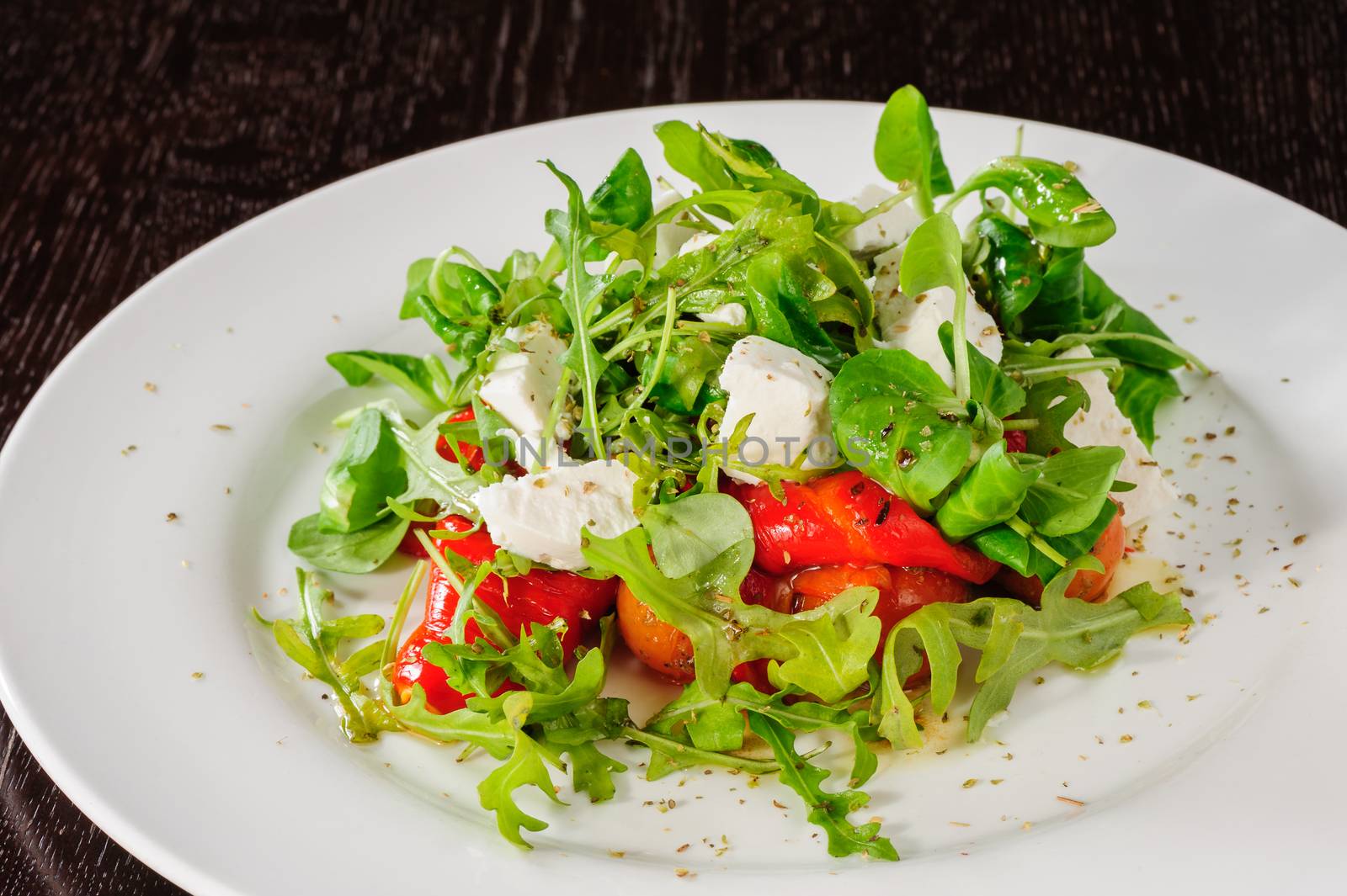 Warm salad with Tomatoes, ruccola, spinach, cooked bell pepper and cheese served on white plate