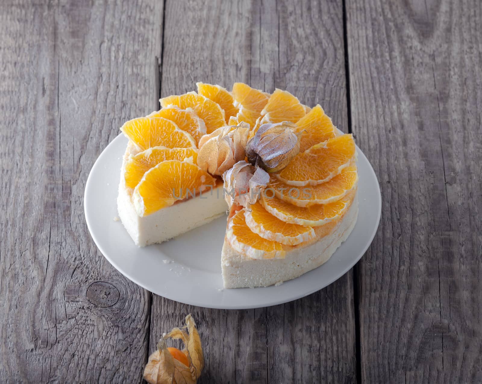 Cheesecake decorated with oranges and physalis on a wooden surface.