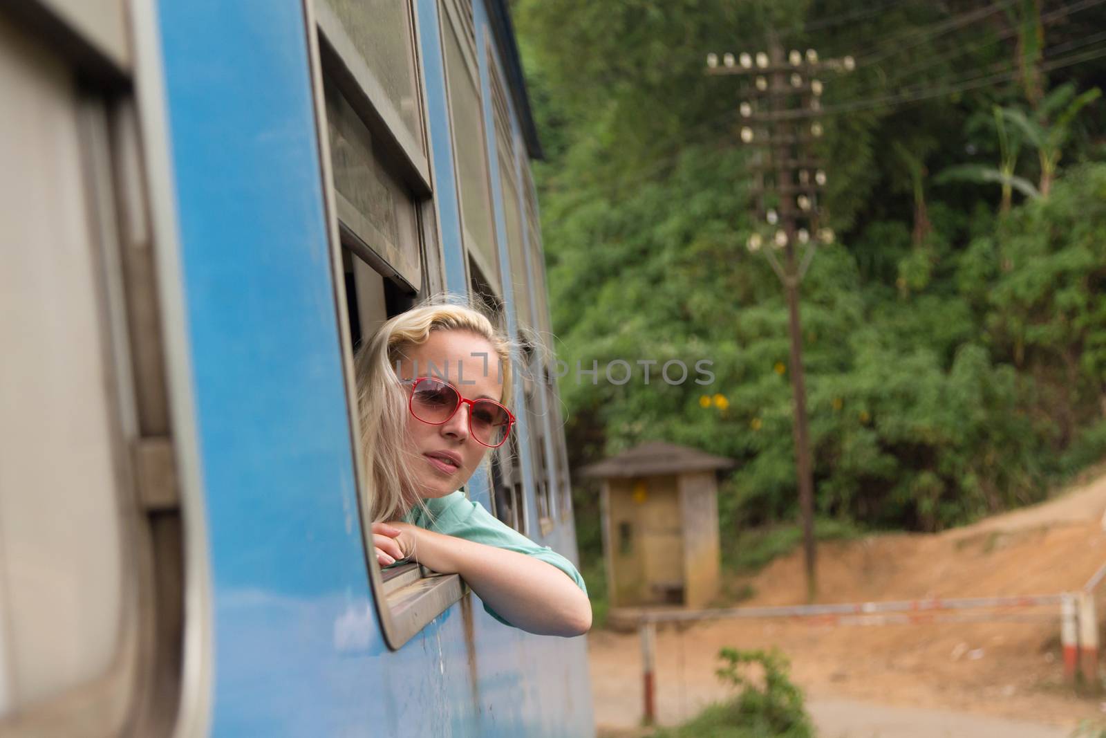 Blonde caucasian woman looking trough old retro blue train window , traveling by train in third world country.