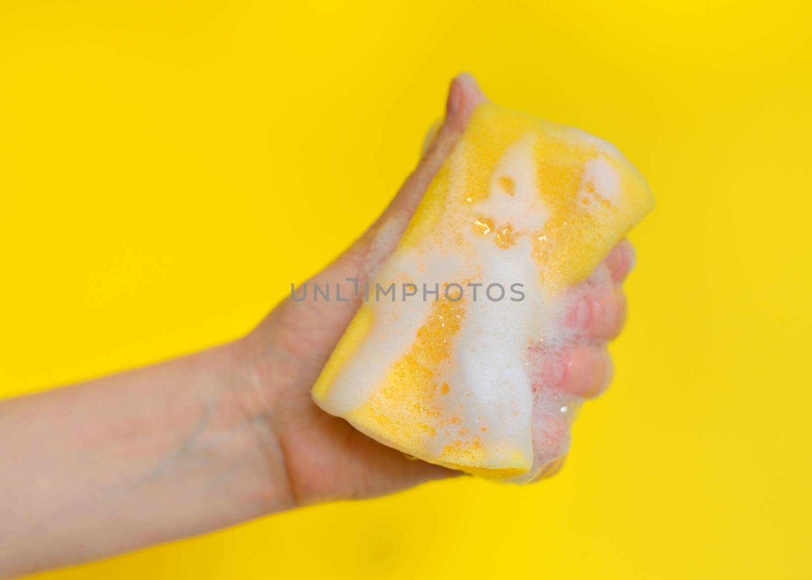 Hand with sponge with foam on yellow background