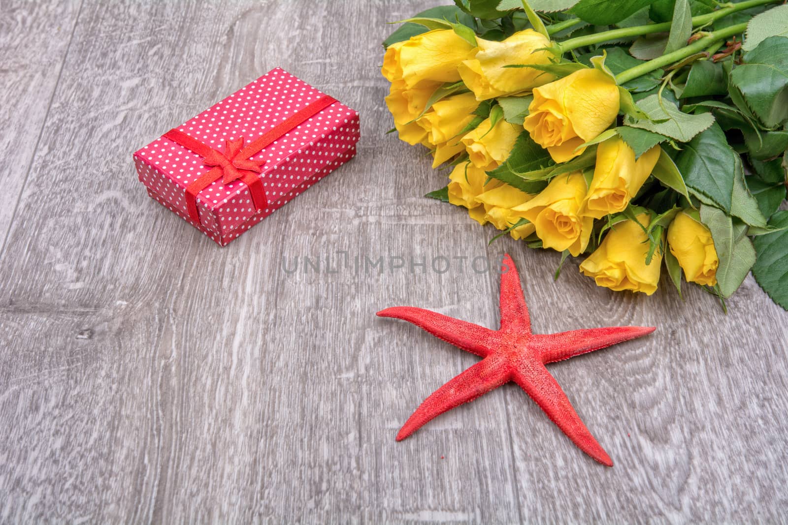 Yellow roses, red gift and red starfish on grey wooden background
