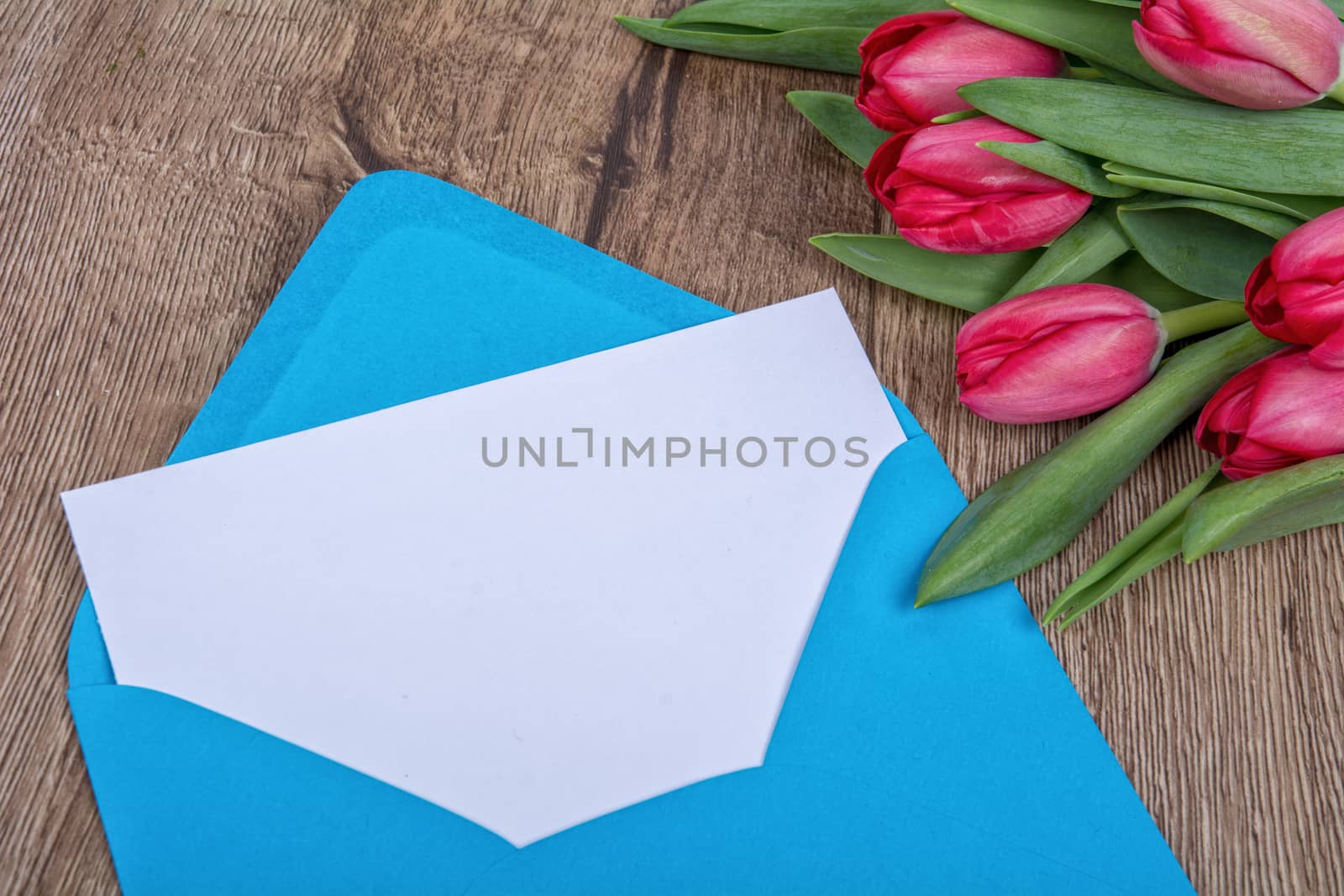Envelope with sheet of paper and red tulips on a wooden background