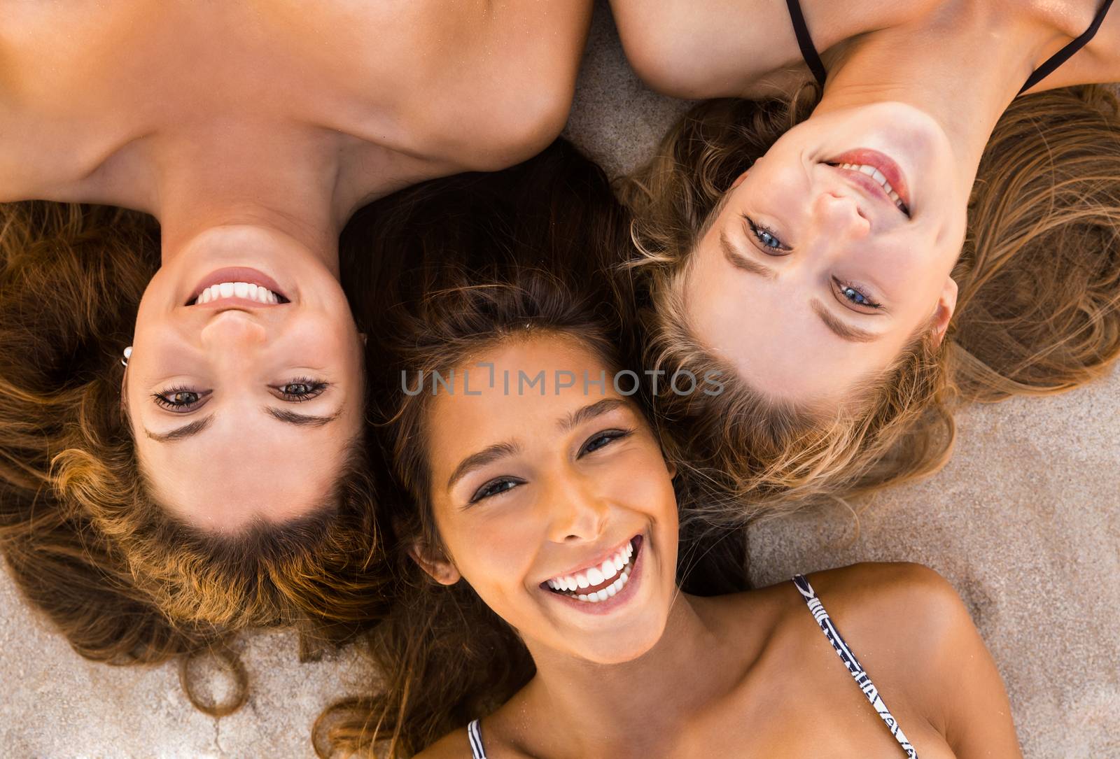 Top view portraits of three beautiful girls on the beach lying on the sand