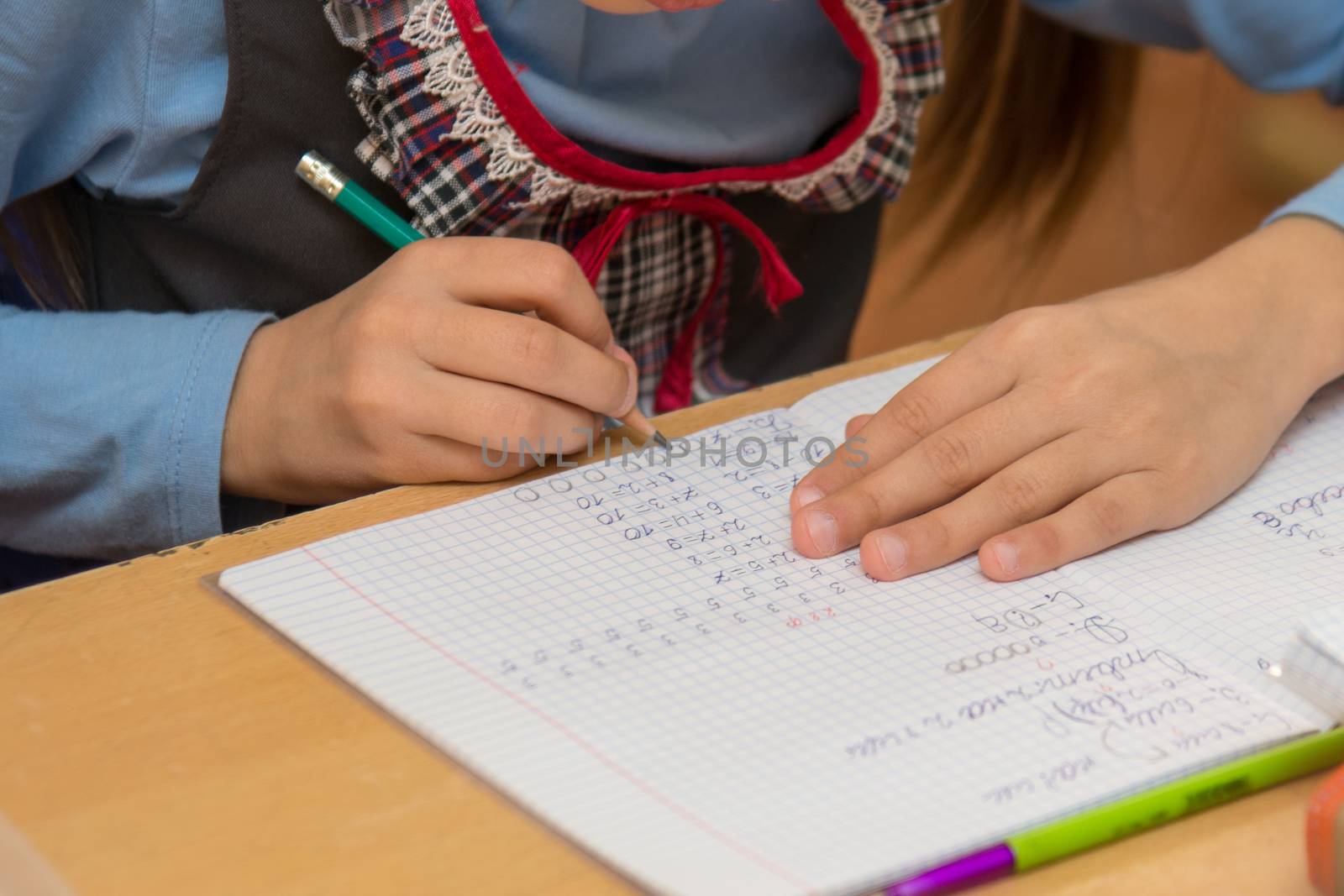 First-grader at a lesson mathematics writes in the notebook, close-up