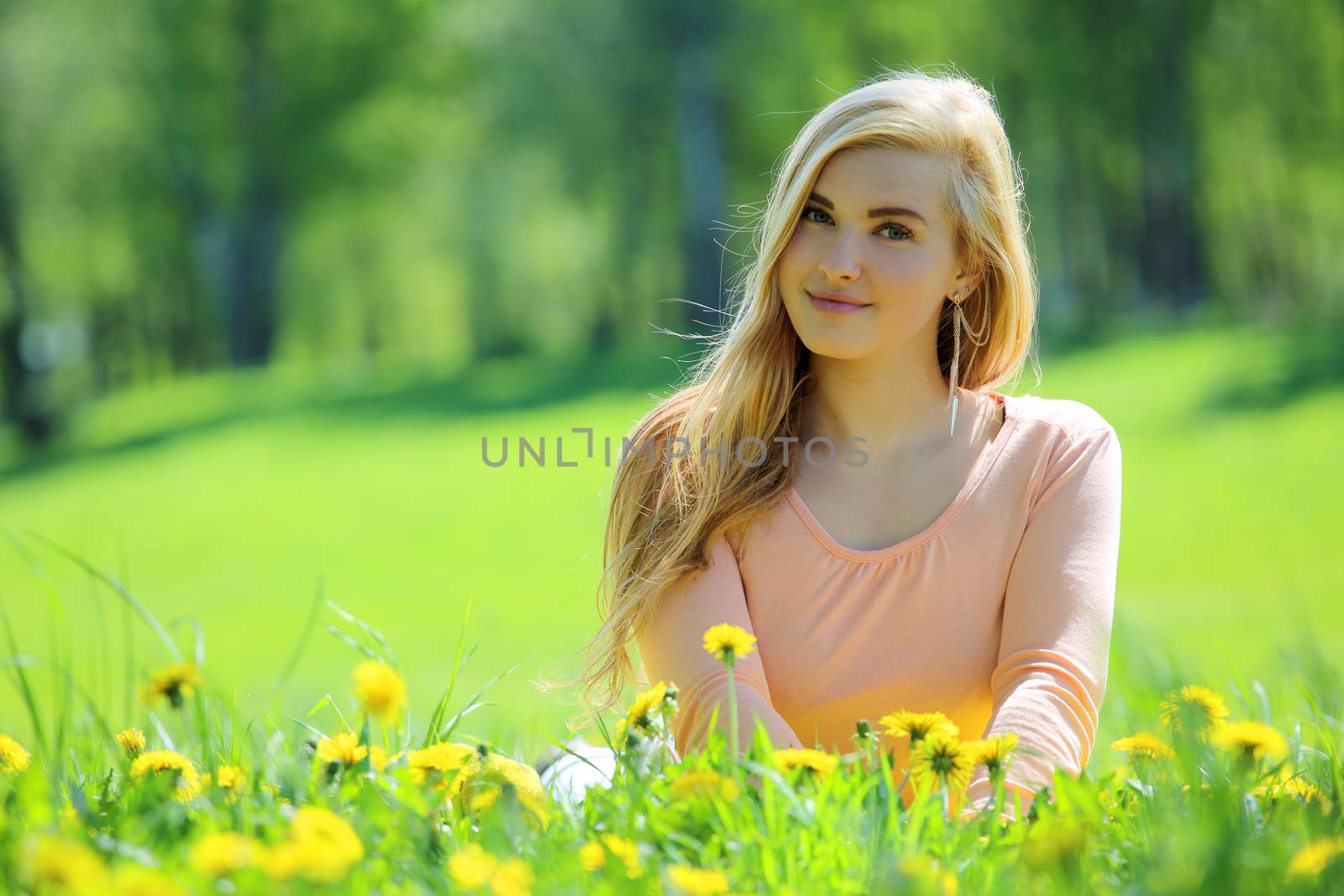 Beautiful young woman laying in spring park with dandelion flowers