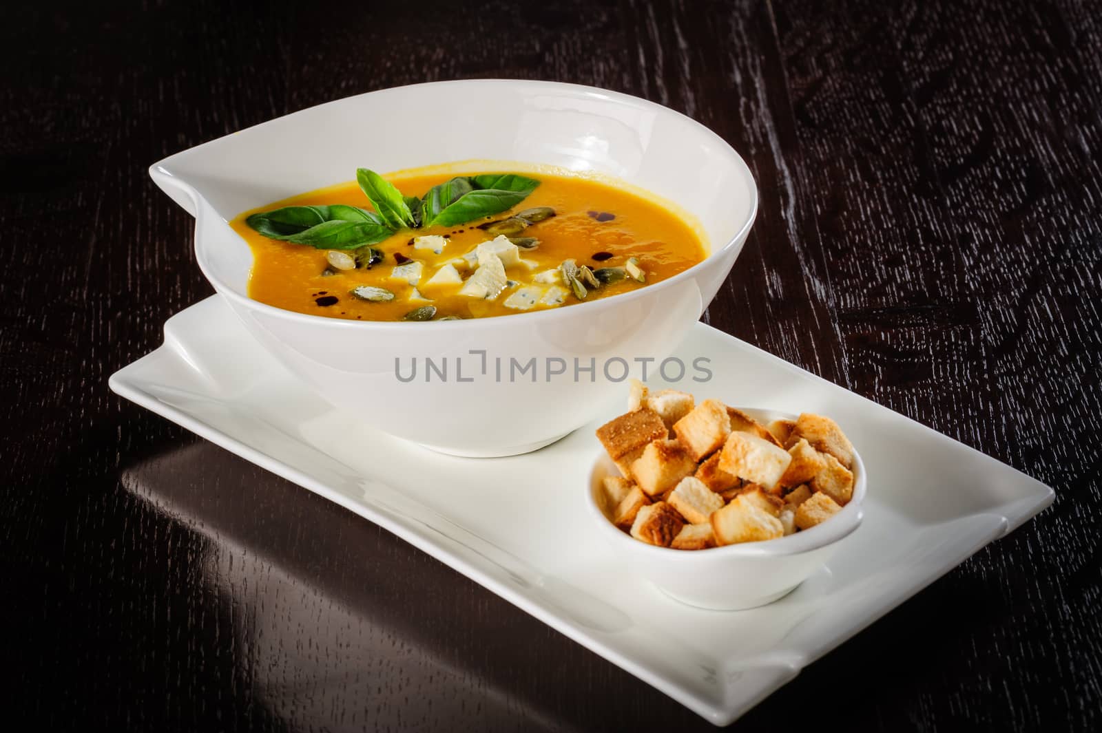 Roasted pumpkin soup with cream and pumpkin seeds on dark wooden background.