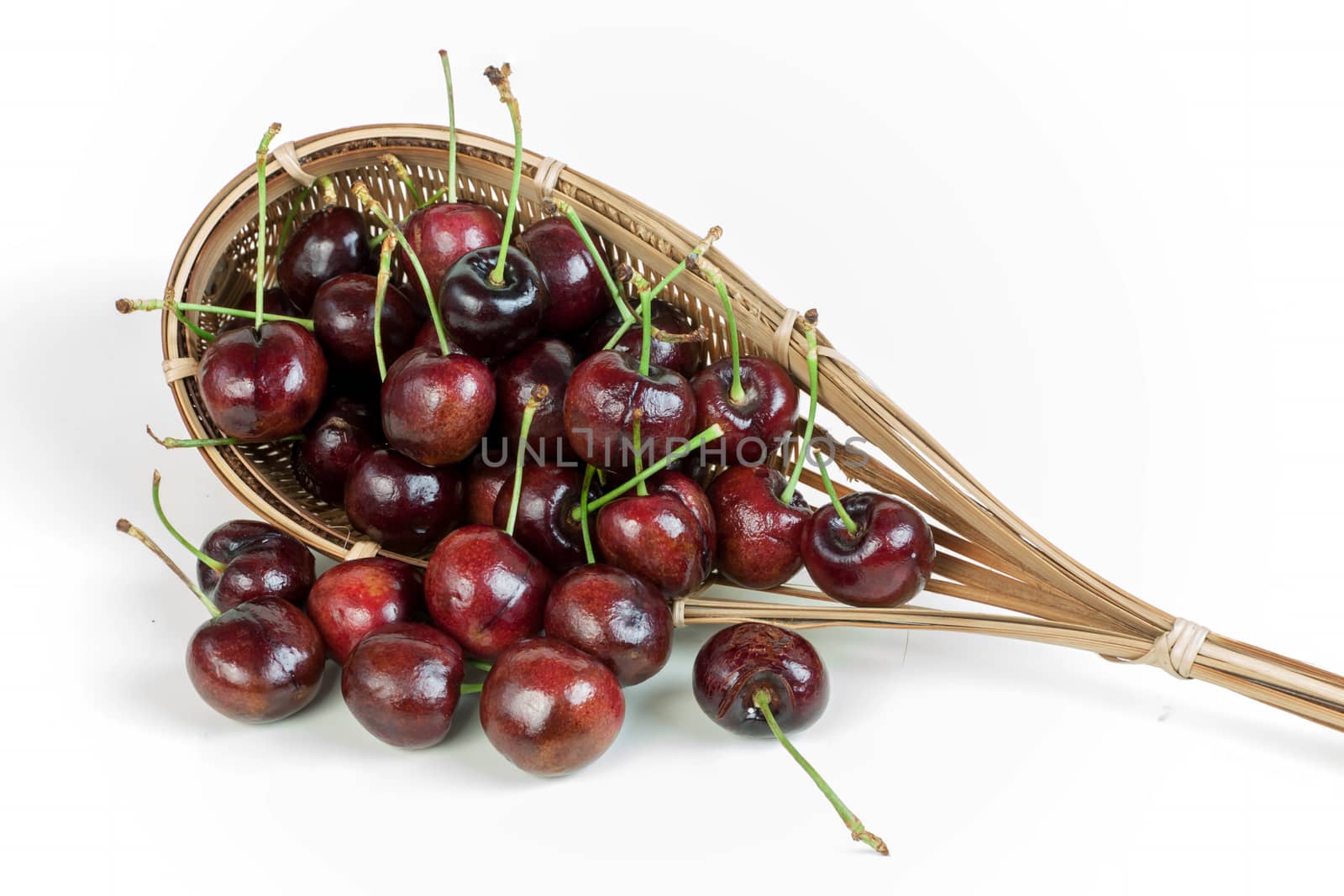 cherries stack in fruit-picker made of a wicker scoop fixed to long handle on white background. 