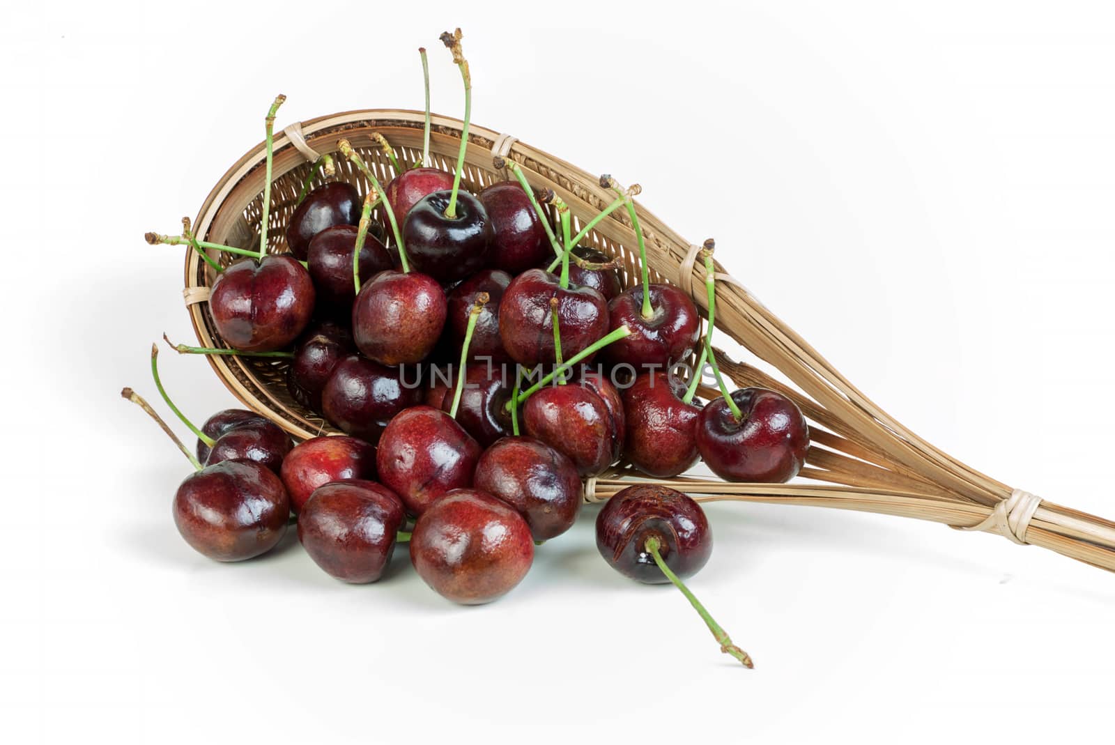 cherries stack in fruit-picker made of a wicker scoop fixed to long handle on white background. 